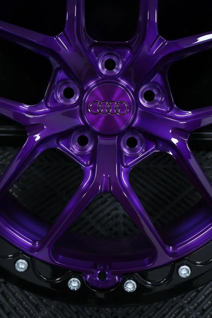 Close-up of a purple Audi car rim with the Audi logo at the center, shiny and illuminated under lighting.