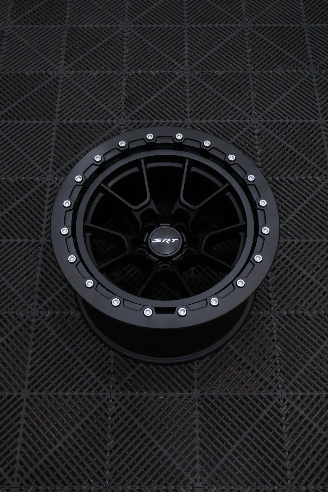 A black SRT branded wheel rim with silver bolts on a black textured surface.