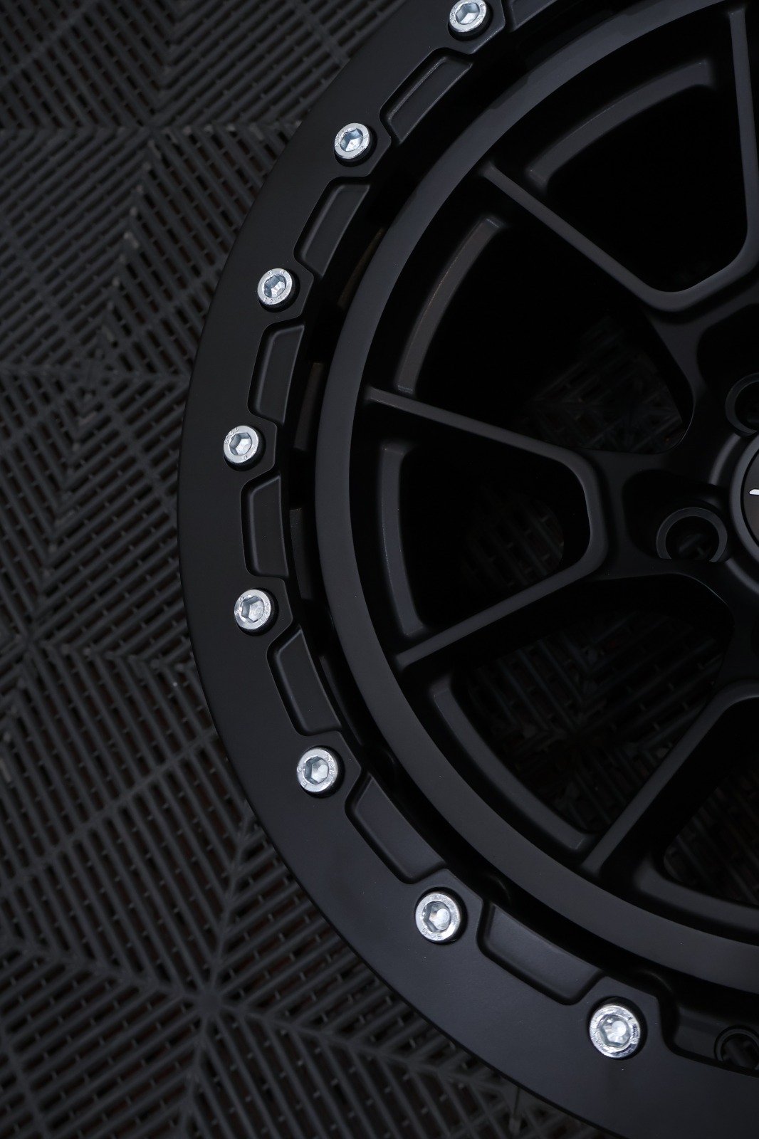 Close-up of a black car wheel with silver bolts on a black rubber mat.