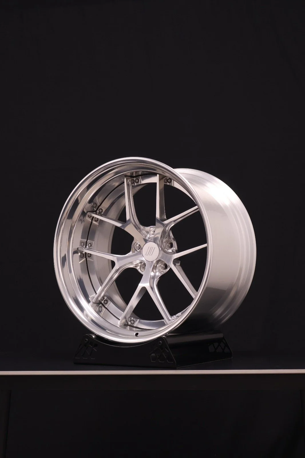 A shiny, silver, multi-spoke car wheel displayed on a black stand against a black background.