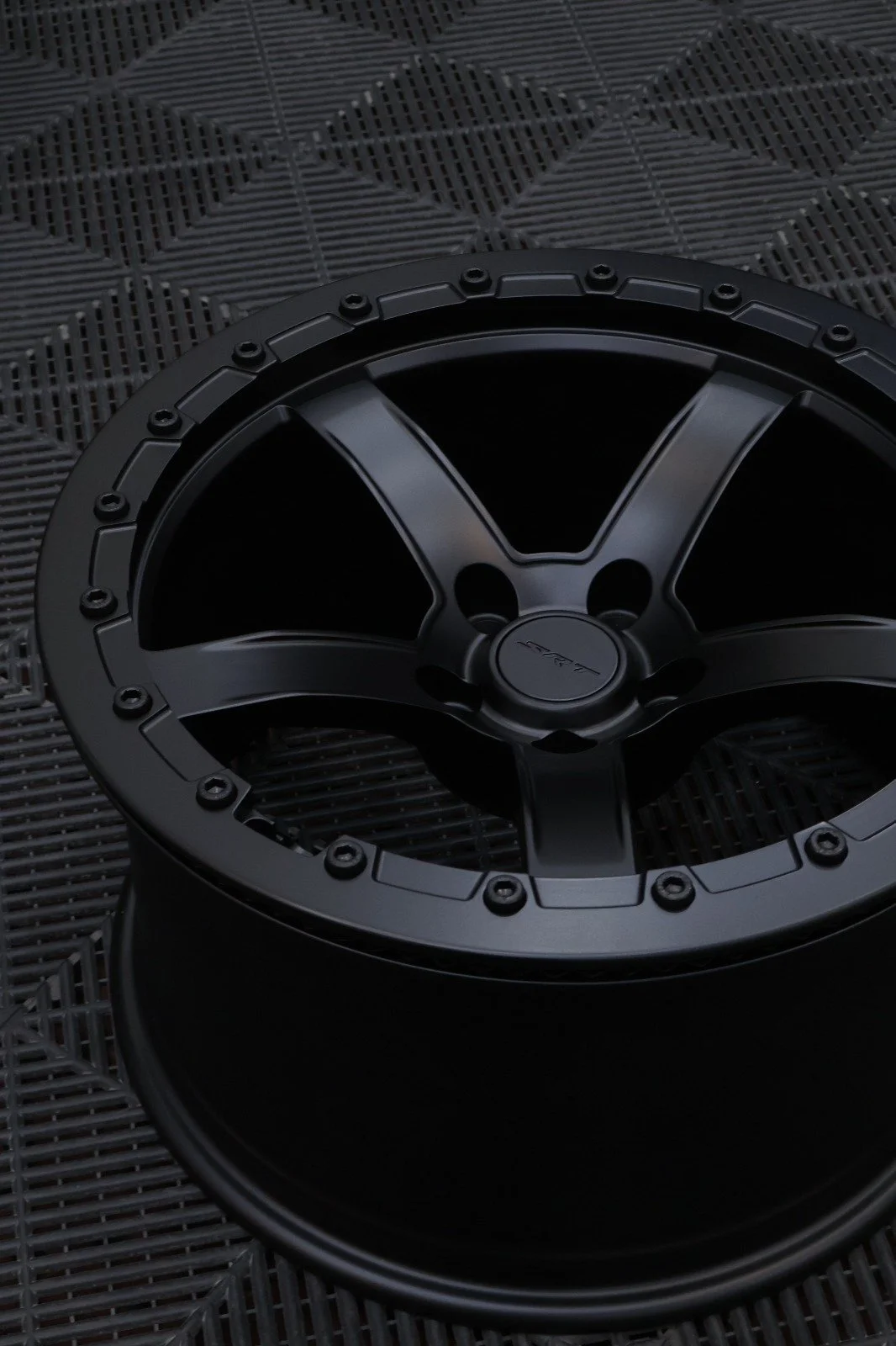 A black car audio subwoofer speaker with a modern design, placed on a textured black surface.