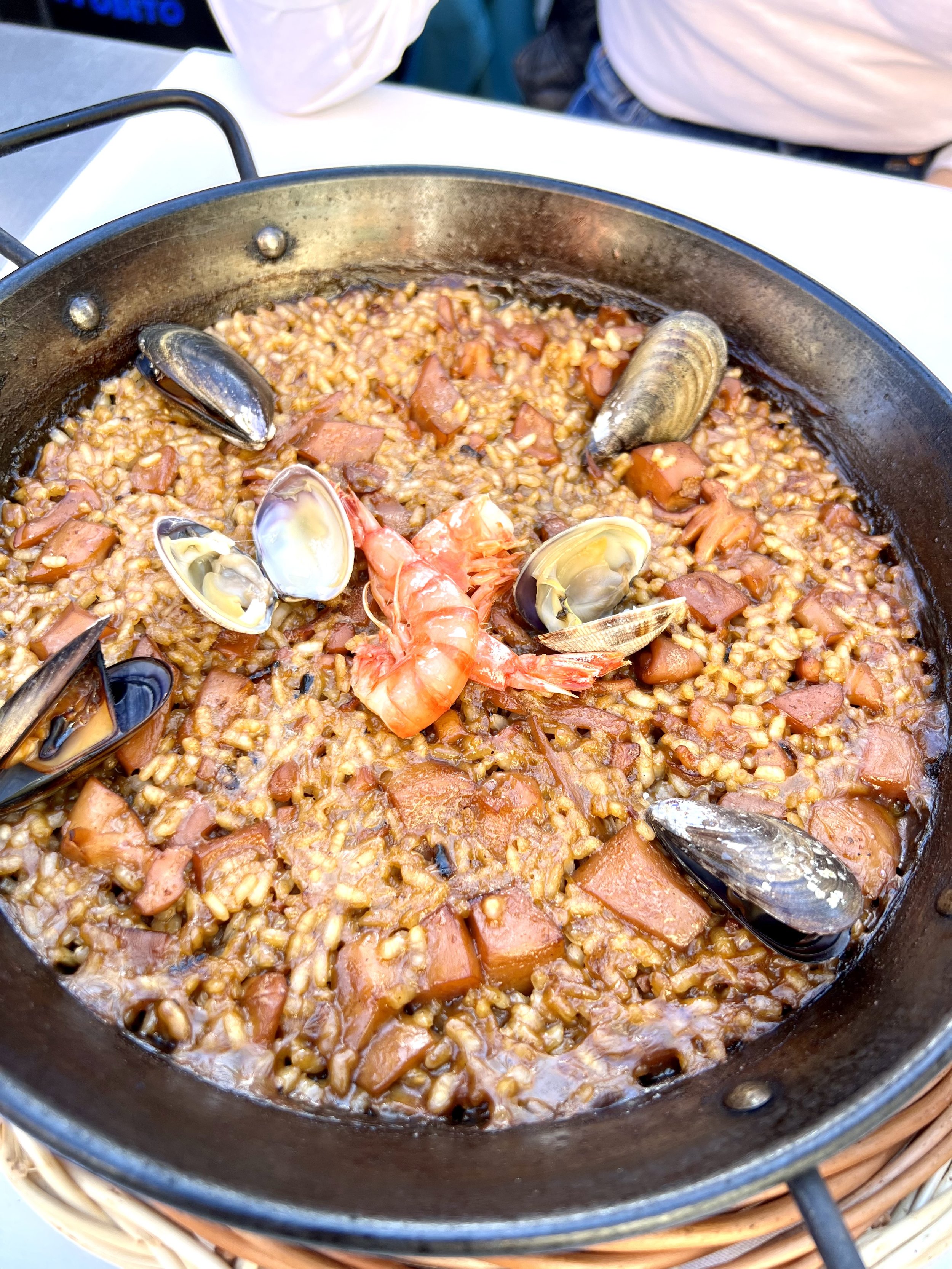 Seafood paella in a black paella pan, featuring rice, shrimp, mussels, and diced ham.