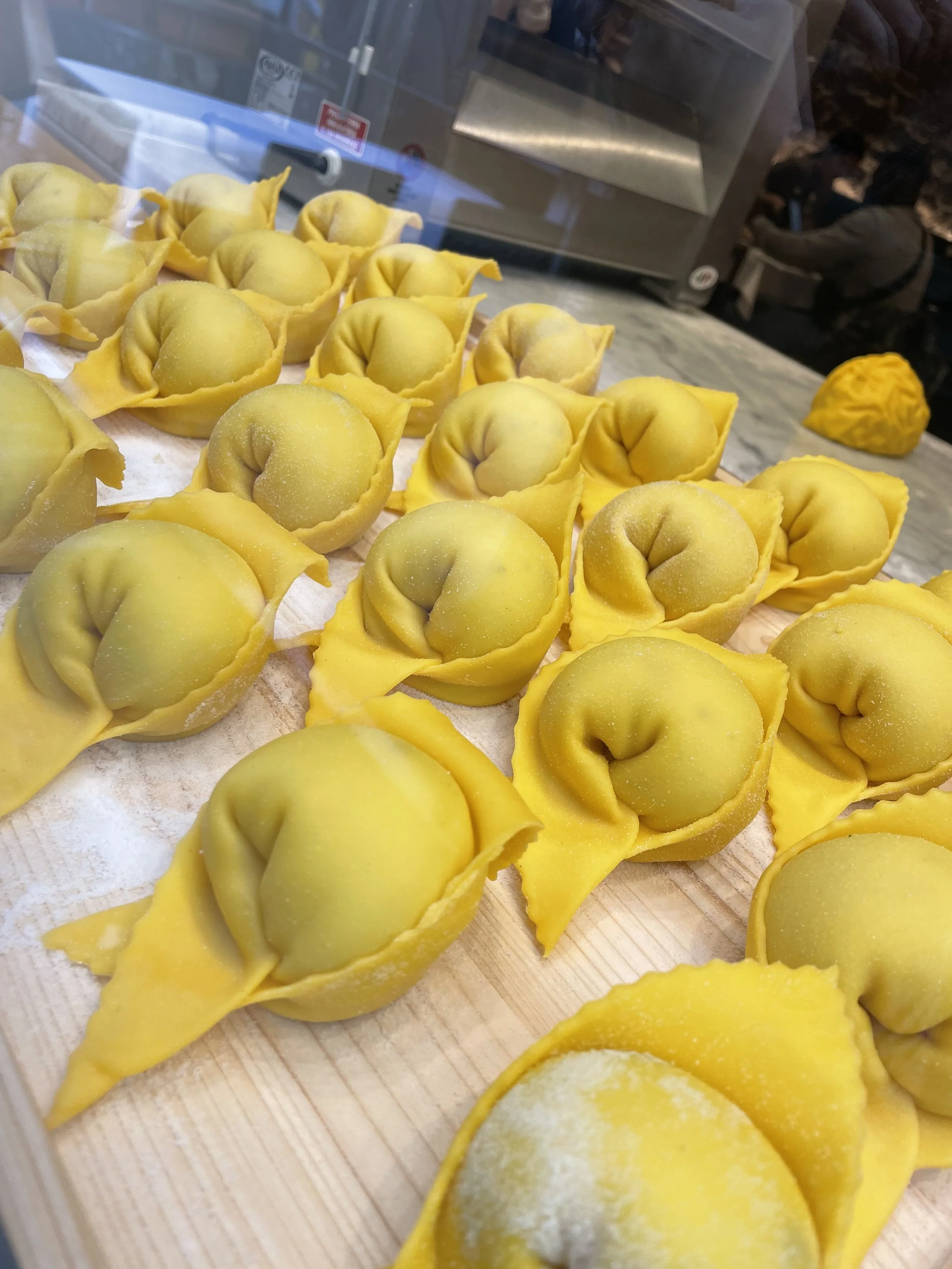 Yellow tortellini pasta with filling, displayed on a wooden surface in a food display case.