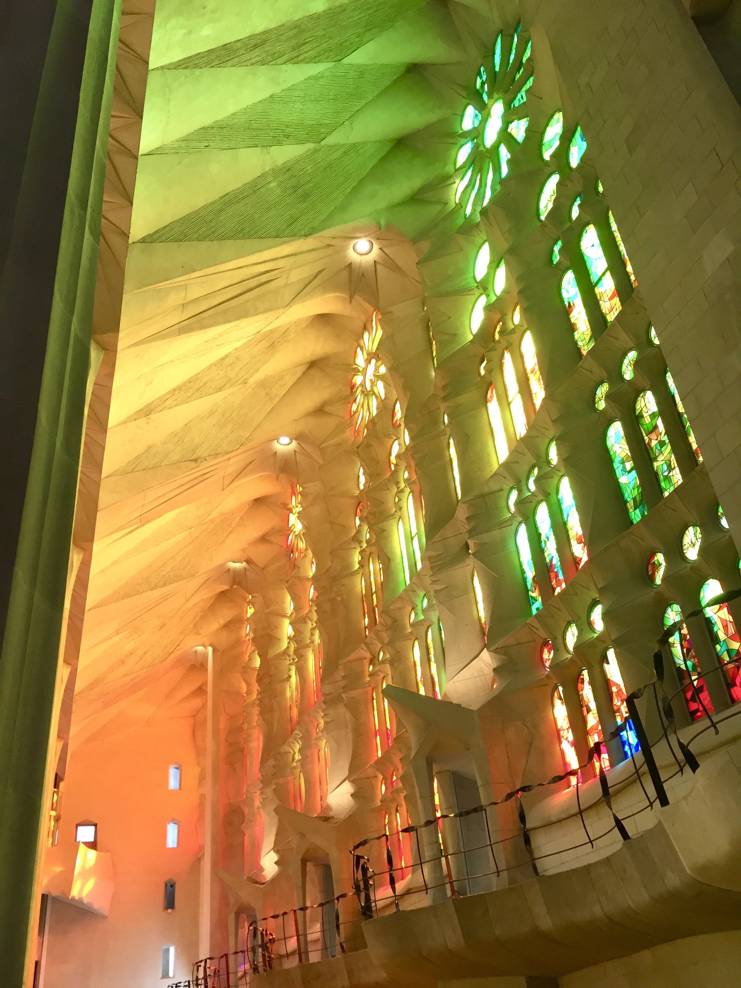 Interior view of the Sagrada Familia church showing colorful stained glass windows and intricate architectural details in warm lighting.
