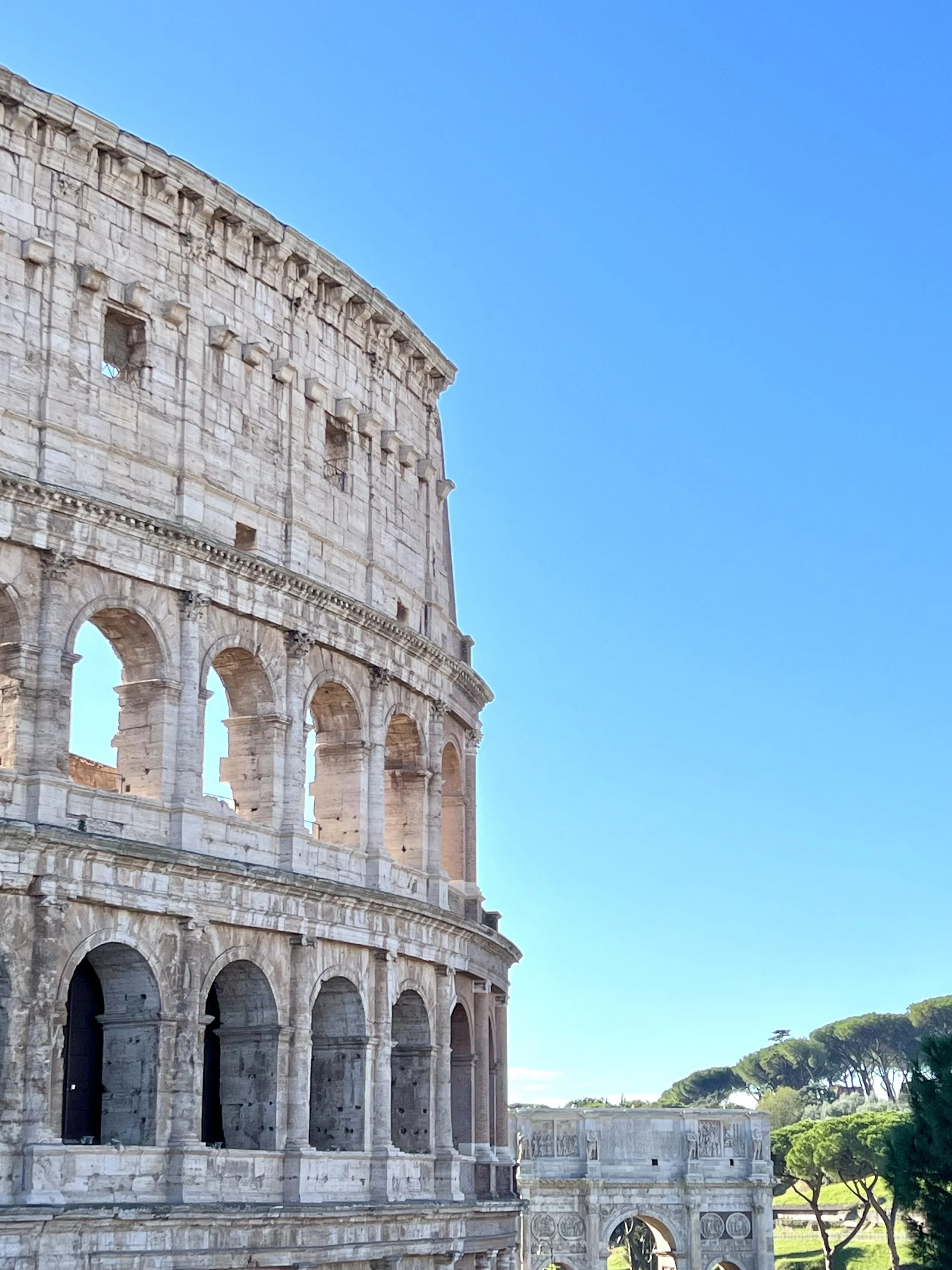 The Colosseum in Rome, Italy, with a clear blue sky and some green trees in the background.