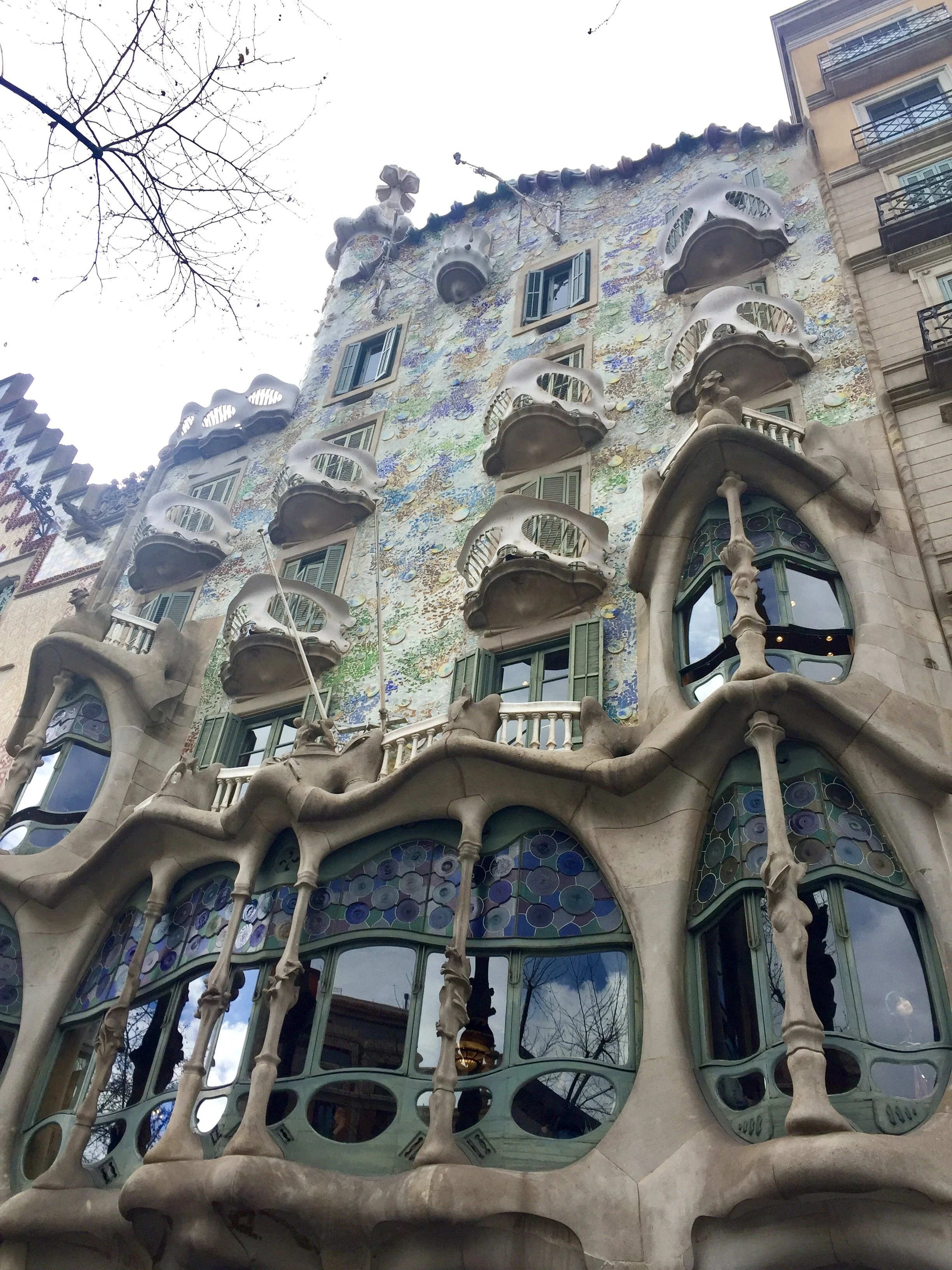 Facade of a colorful, ornate building with organic, flowing architectural details, balconies, and stained glass windows, designed by architect Antoni Gaudí.