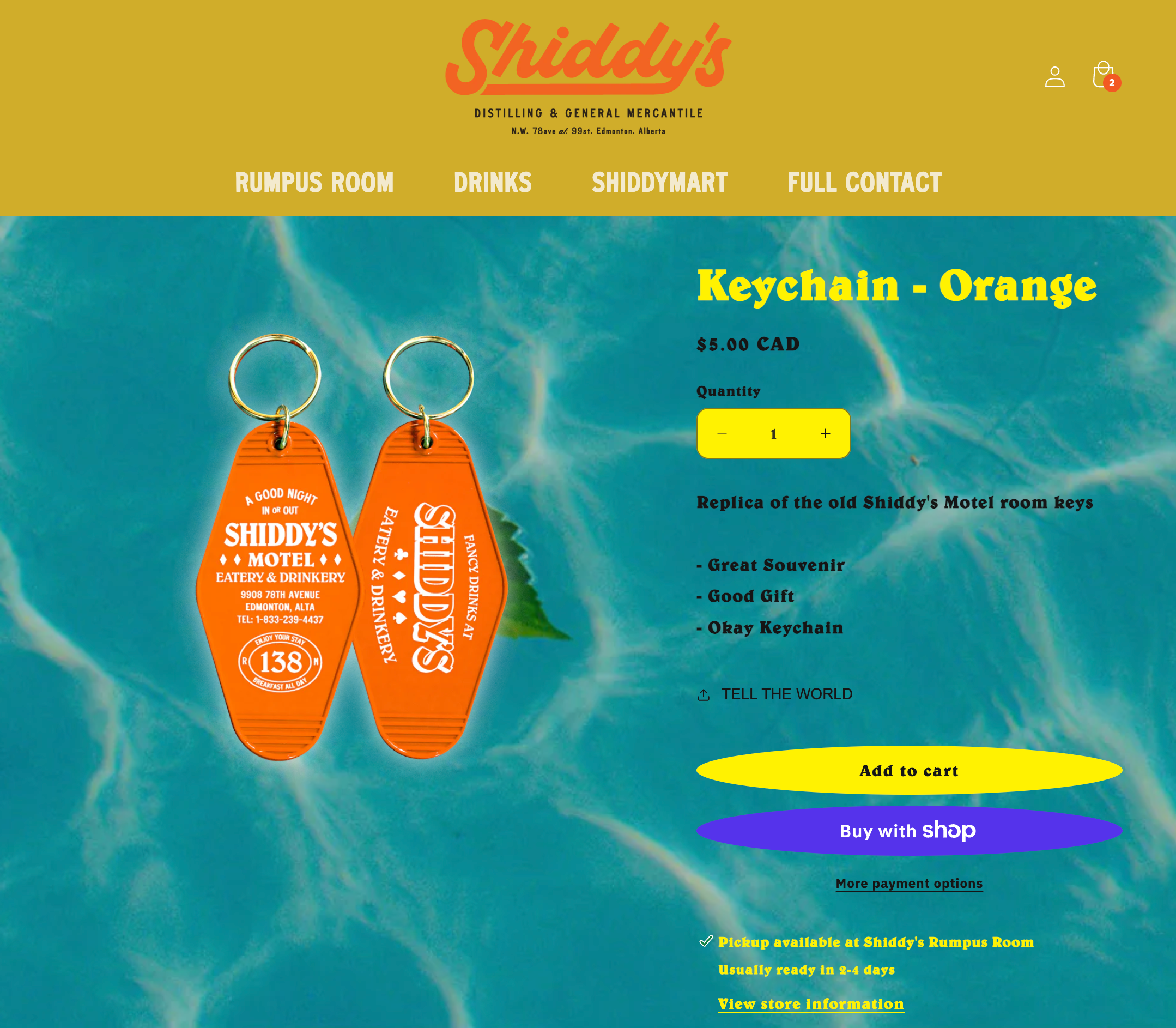 Online shop page for a keychain shaped like a motel room key from Shiddy’s Motel, in orange color, with details including price, quantity selection, and add to cart button.
