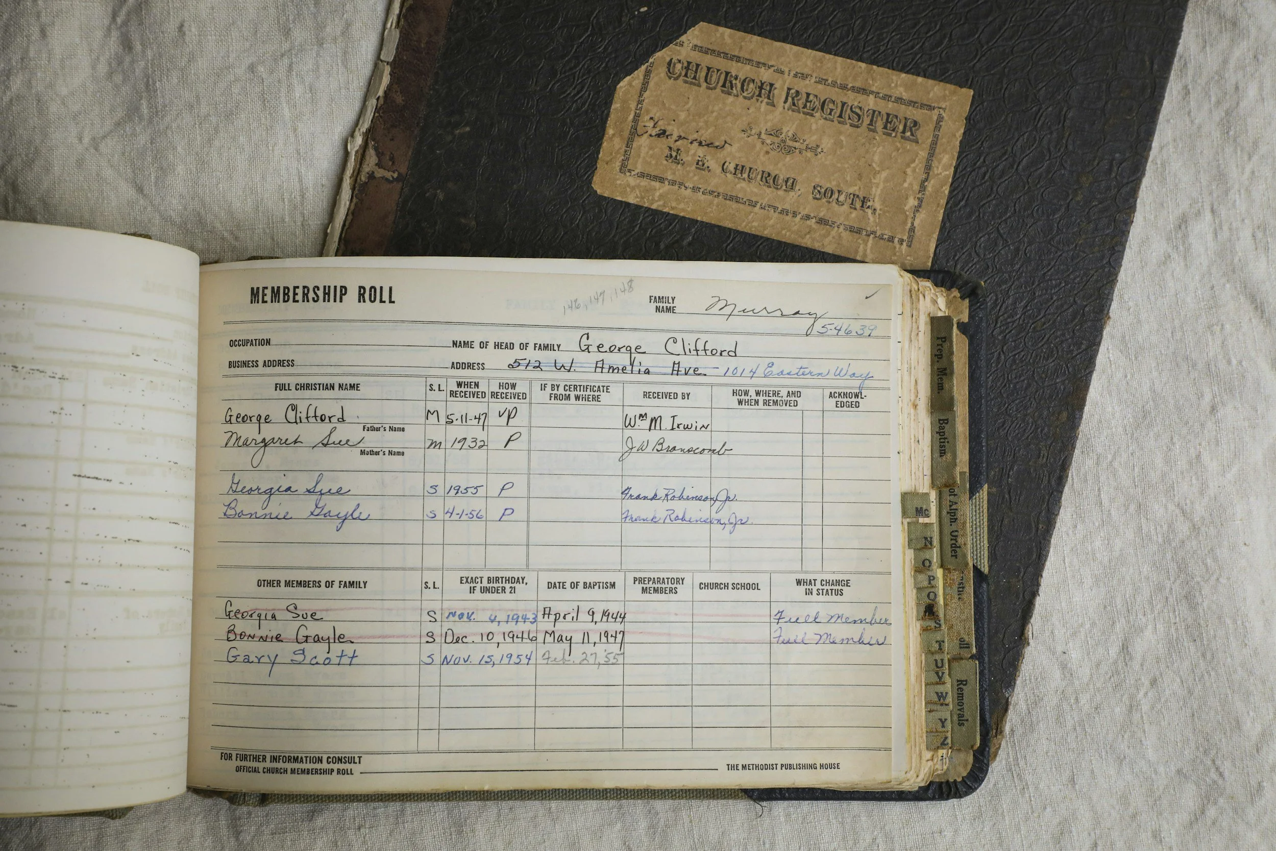 Open church register book showing handwritten entries for a family, with names, addresses and dates recorded on aged paper with alphabetical tabs.