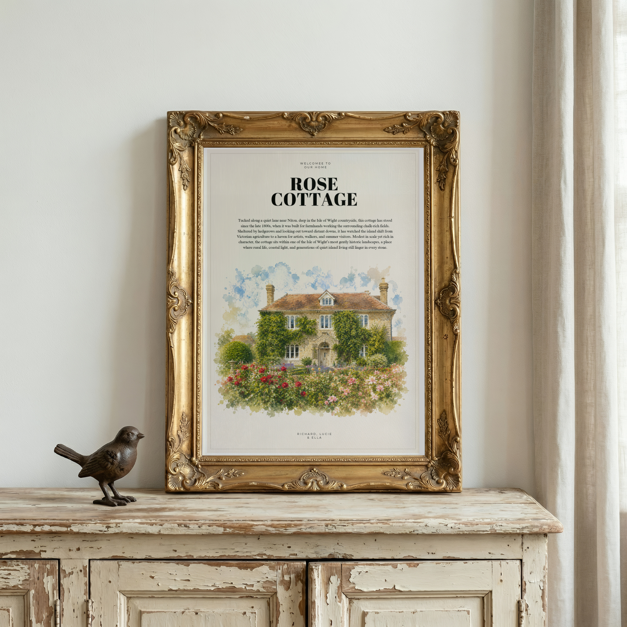 Framed illustration of ‘Rose Cottage’ in an ornate gold frame on a distressed wooden cabinet beside a small bird figurine.