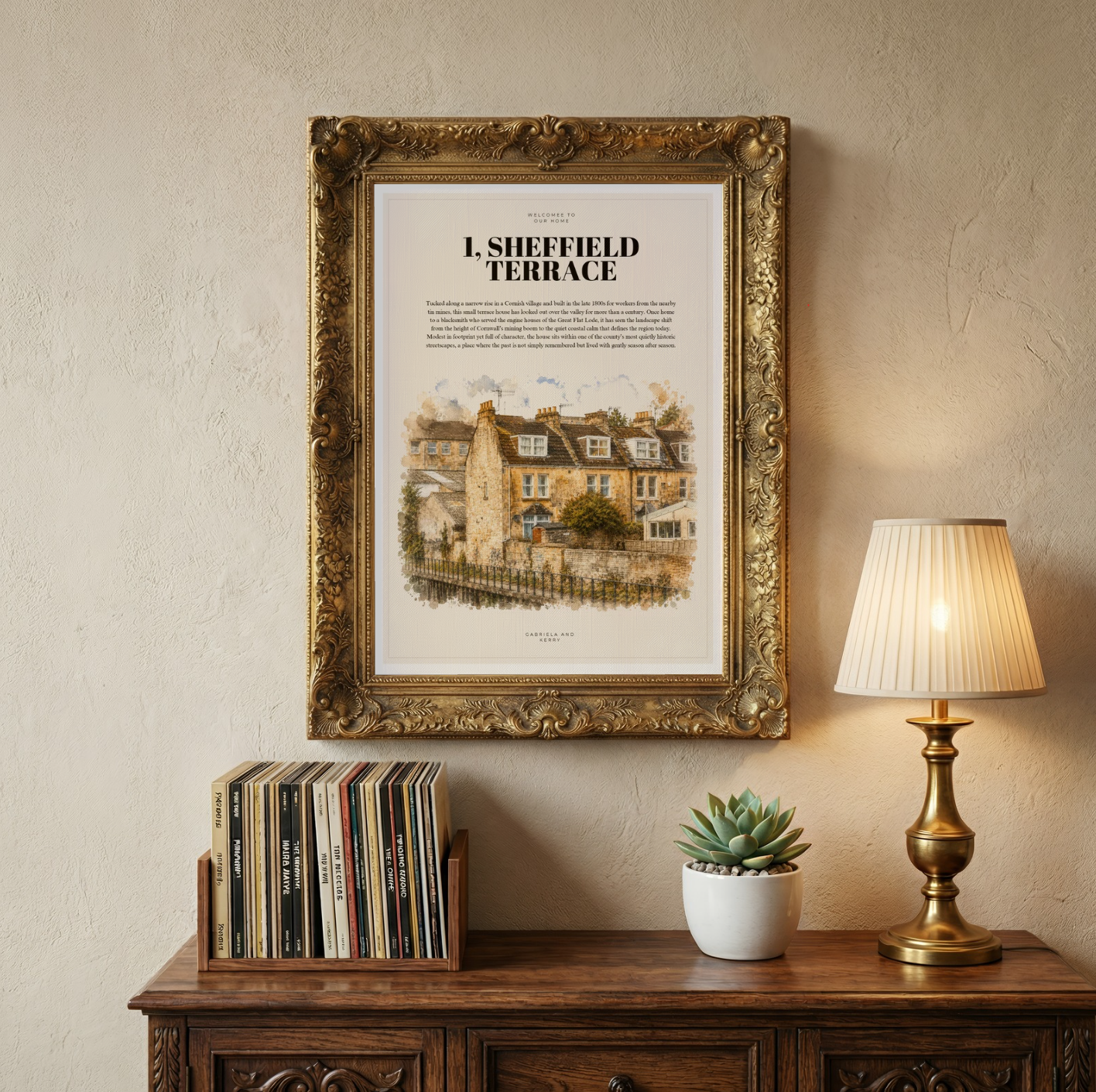 Framed illustration of ‘1 Sheffield Terrace’ displayed above a wooden cabinet with books, a lamp and a small potted plant.