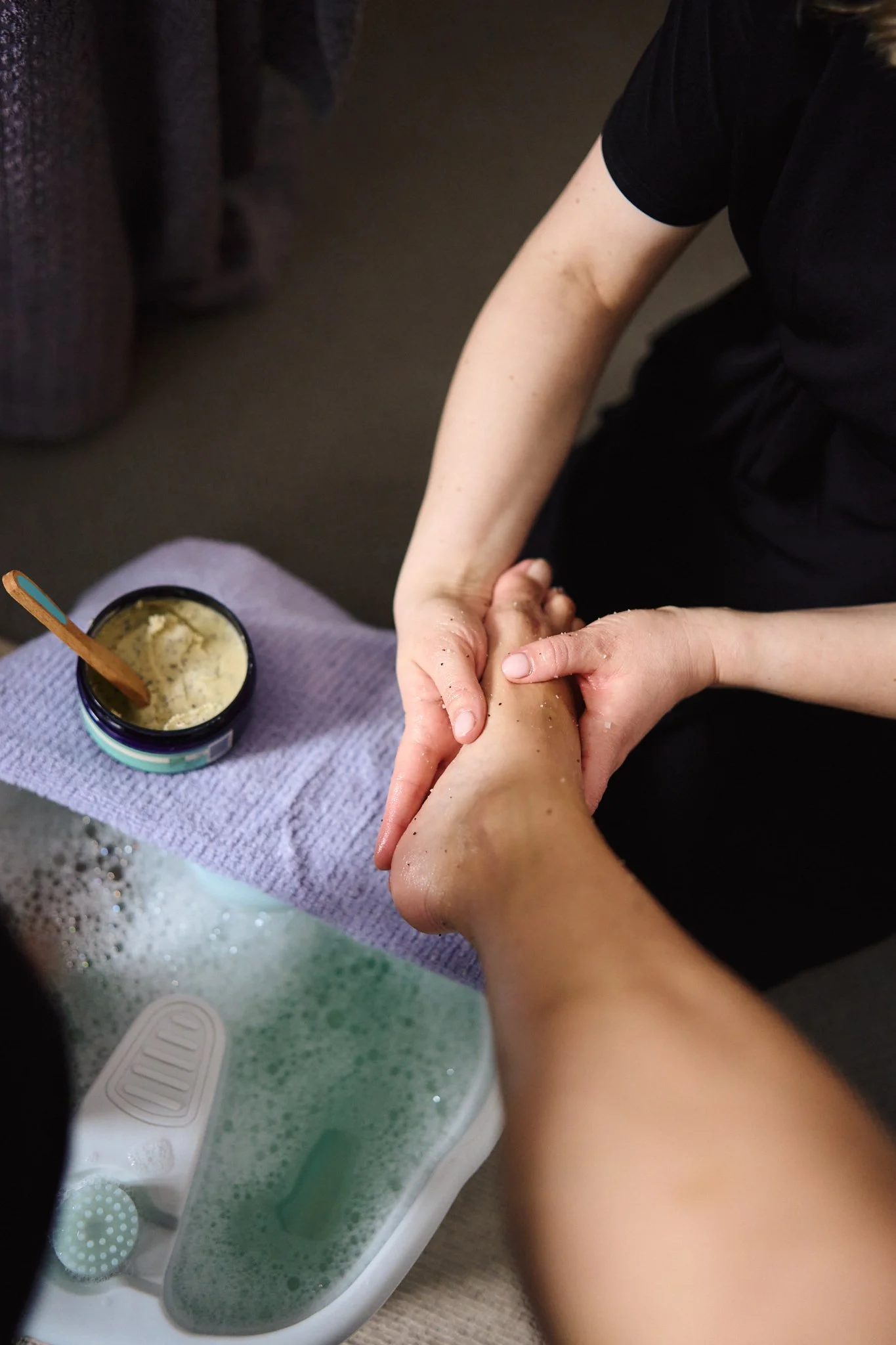 Massage therapist Gabriella Bloom providing a relaxing foot soak and scrub to start a facial massage in her serene home spa setup in Fleet, Hampshire.