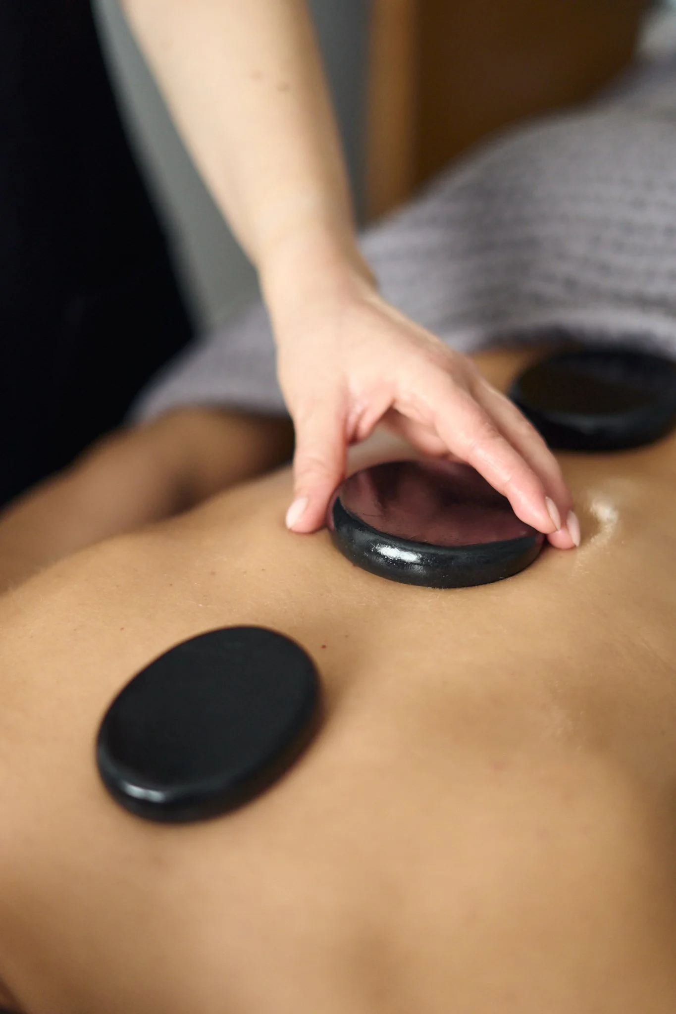 Massage therapist Gabriella Bloom providing a relaxing hot stone massage as part of a massage and facial ritual in her serene home spa setup in Fleet, Hampshire.