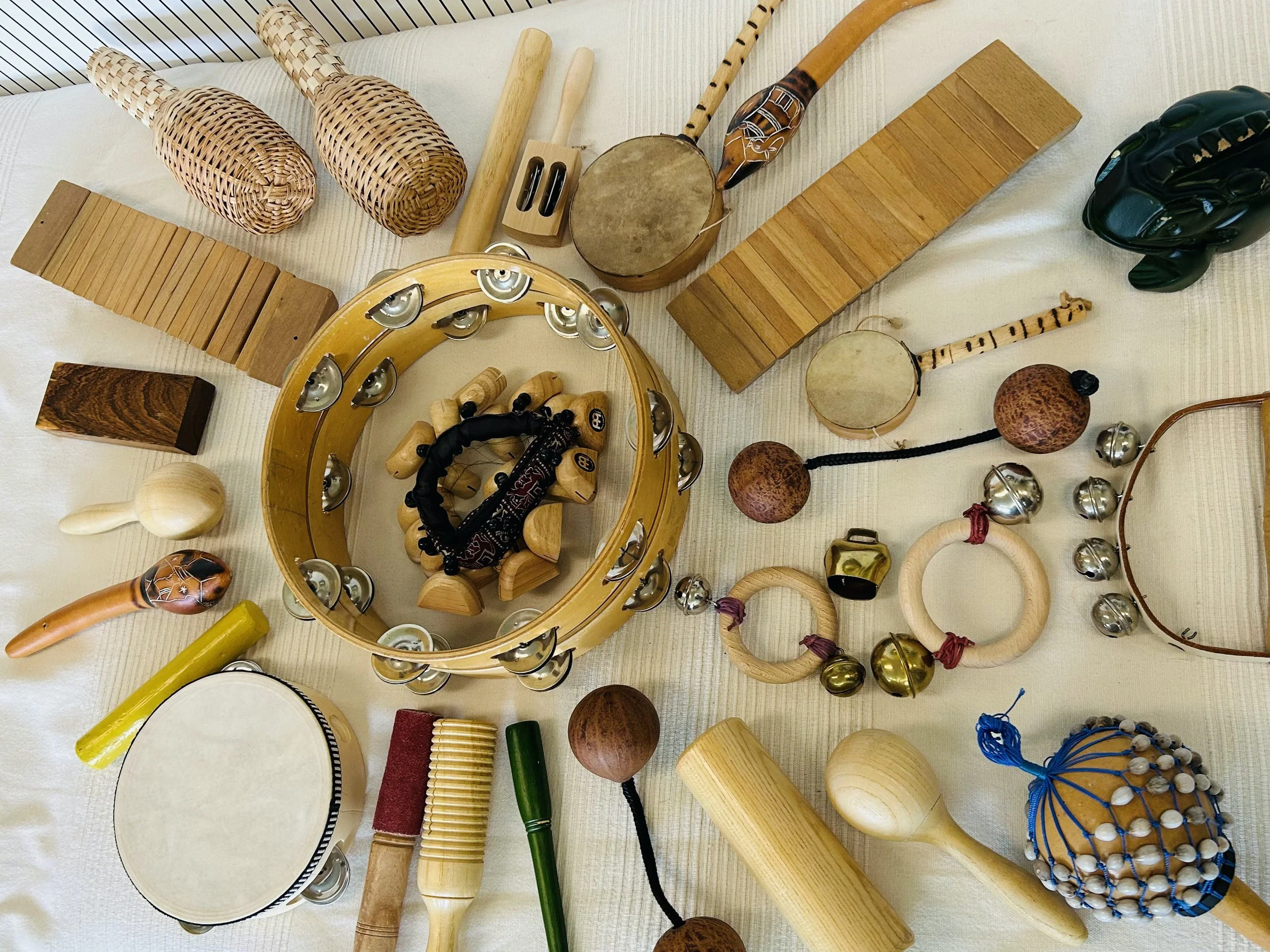 Verschiedene Percussion-Instrumente auf einem weißen Bettlaken, darunter Trommeln, Rasseln, Maracas, Riemen, und andere Schlaginstrumente.