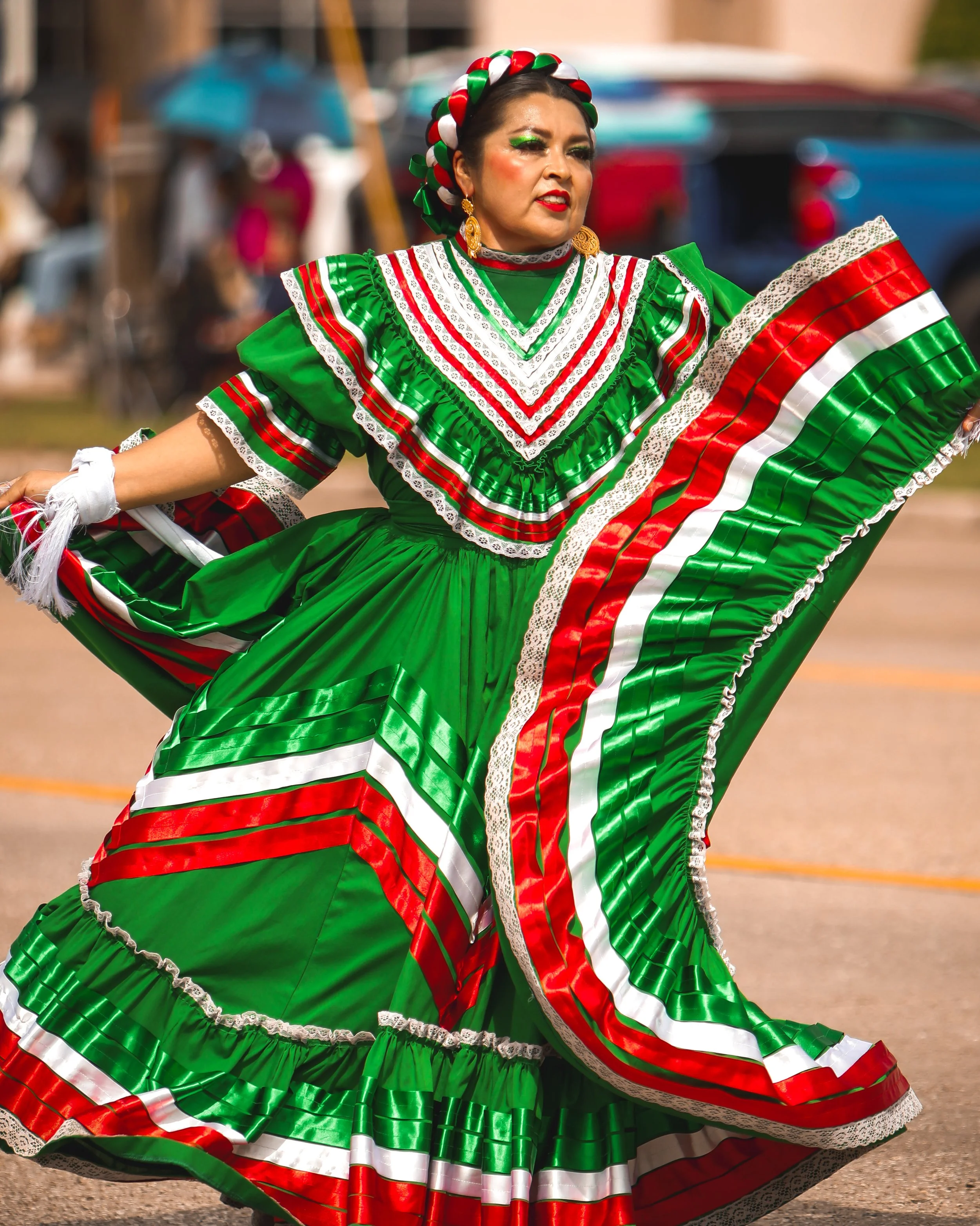 Woman dressed in a traditional Mexican folk dance dress with green, red, white, and lace details, performing a folkloric dance at an outdoor event.