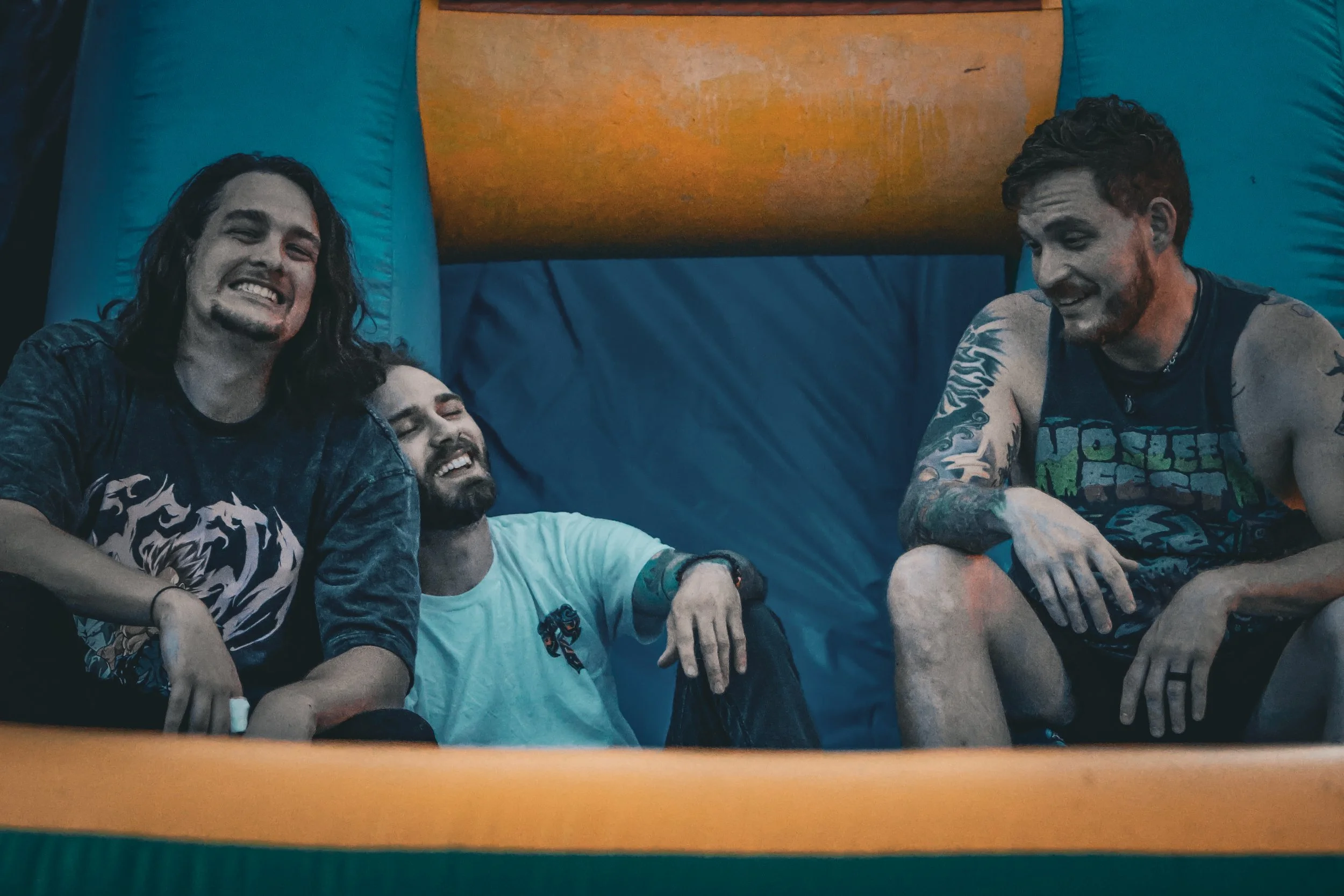 Four men sitting inside an inflatable bounce house, laughing and enjoying themselves.