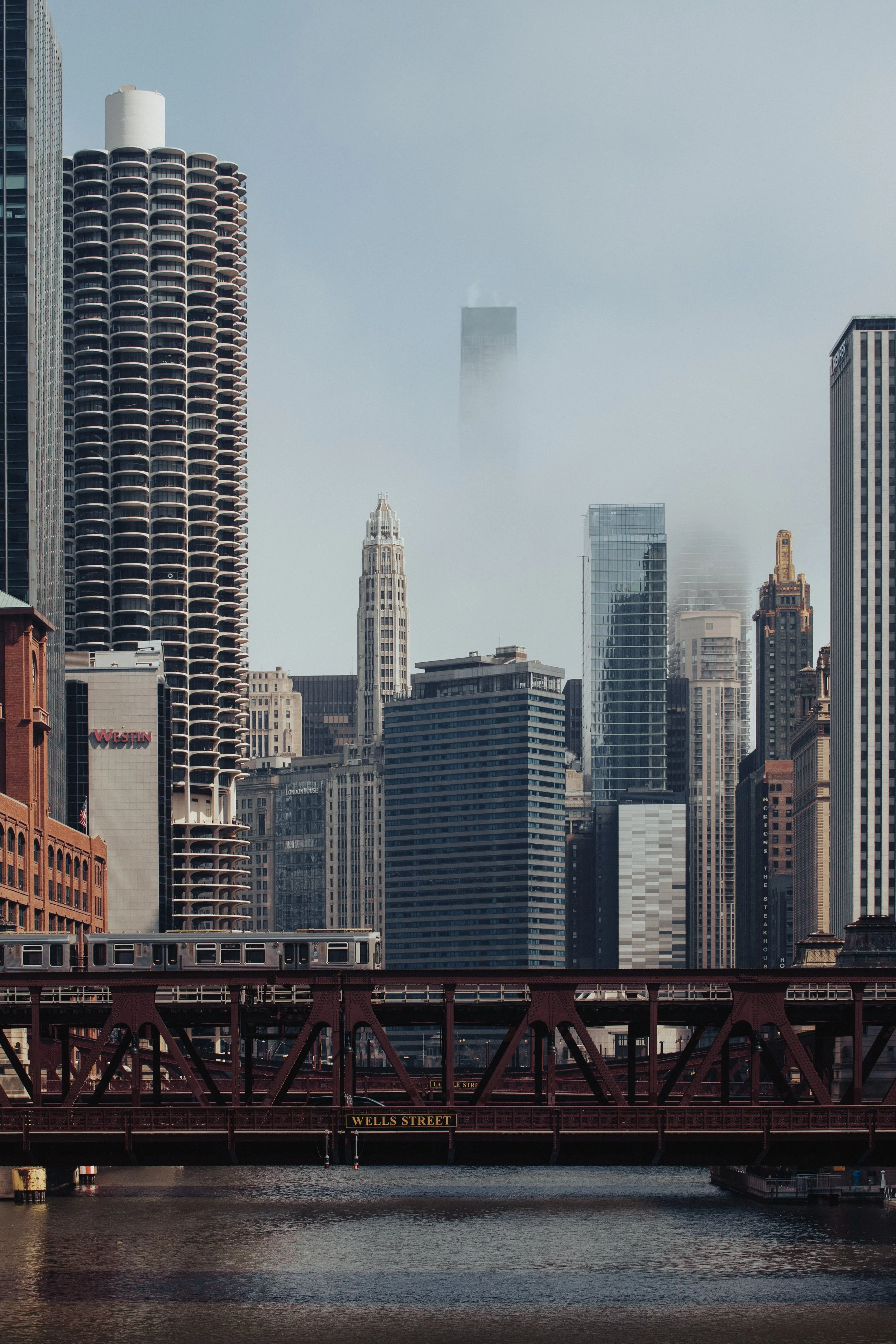 View of Chicago skyline with tall buildings, including the Marina City towers, under a cloudy sky with a bridge labeled 'Wells Street' crossing the river in the foreground.