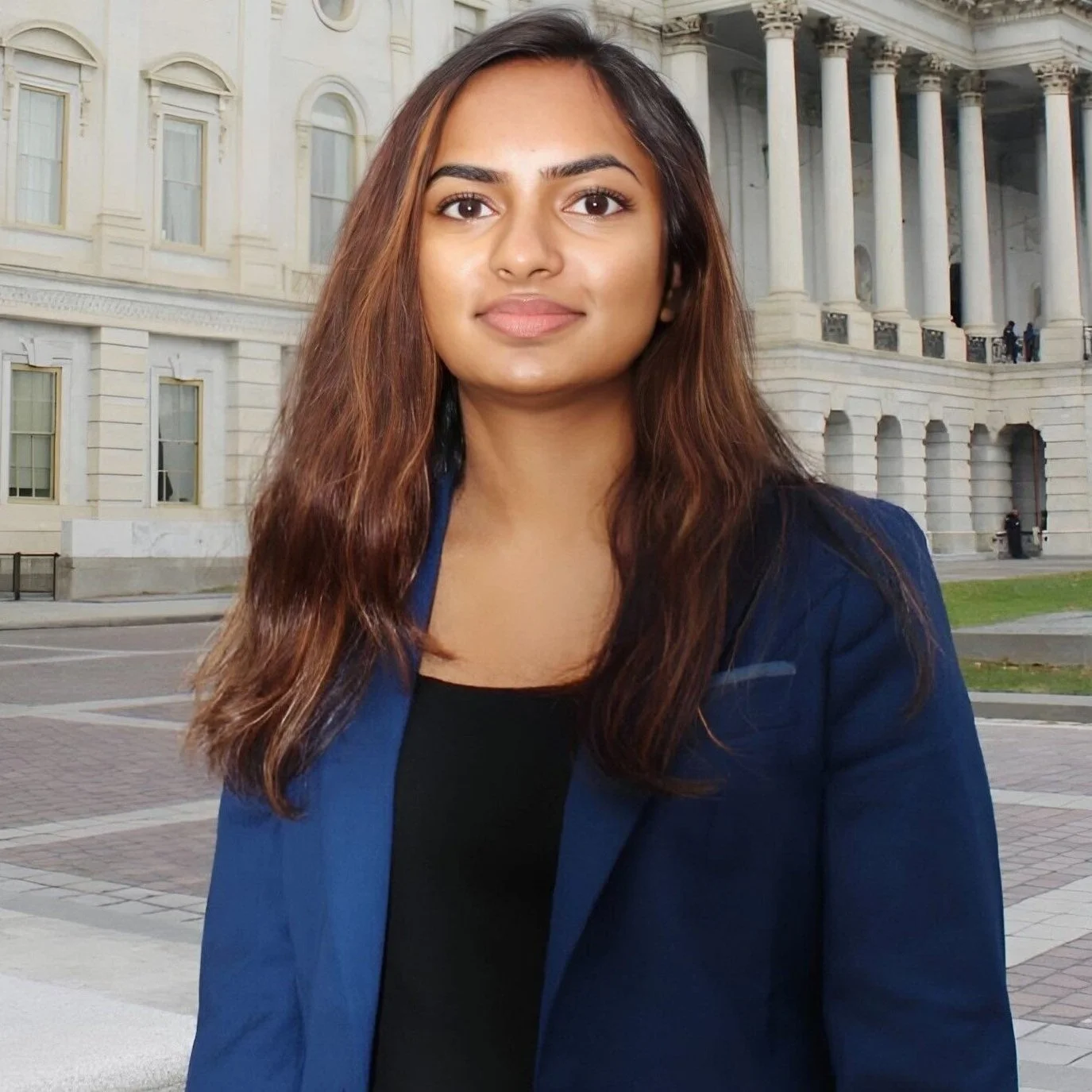 A woman with long, wavy brown hair and a blue blazer standing outside in front of a government building with columns.