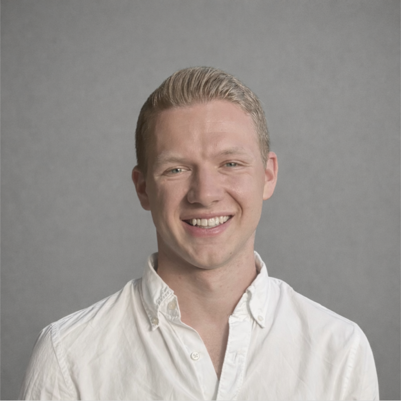A smiling young man in a white button-up shirt against a neutral gray background.