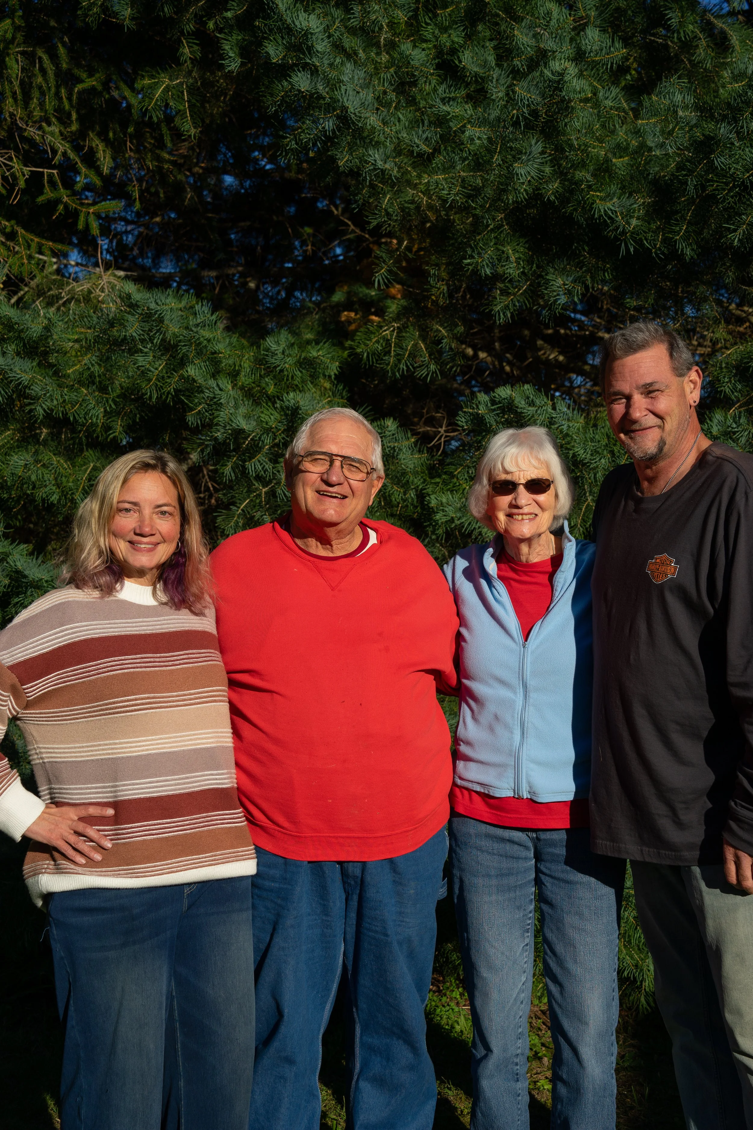 Group of four people standing outside in front of a large green tree, smiling at the camera.
