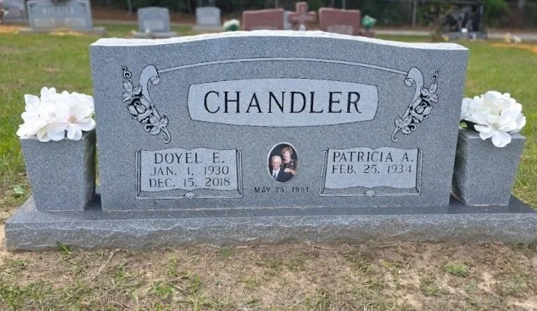Gravestone with two flower pots, a photo in the center, and engraved names and dates.