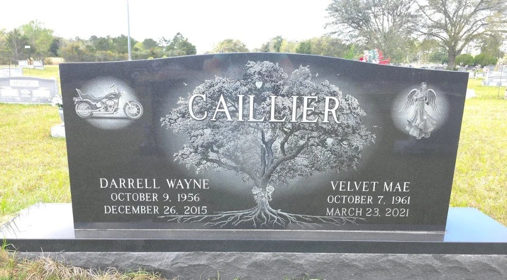 A black granite headstone with a tree engraved in the center, flanked by a motorcycle on the left and an angel on the right.