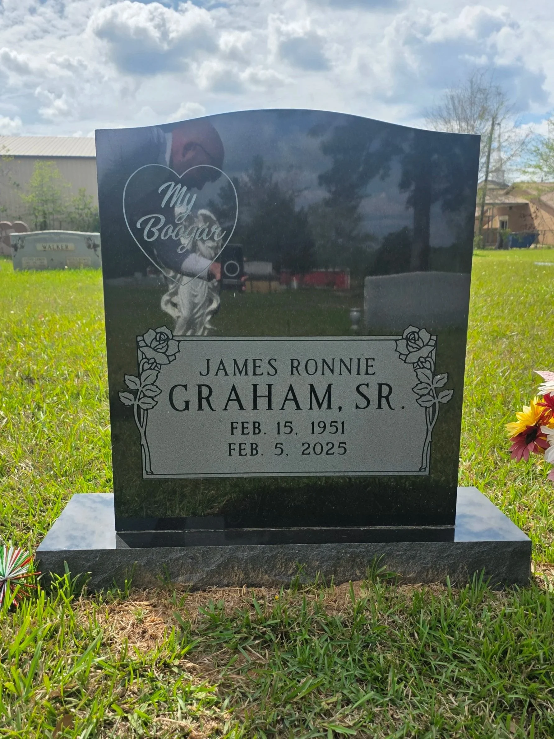 Black polished granite headstone with engraved text and decorative floral corners and a heart-shaped emblem at the top.