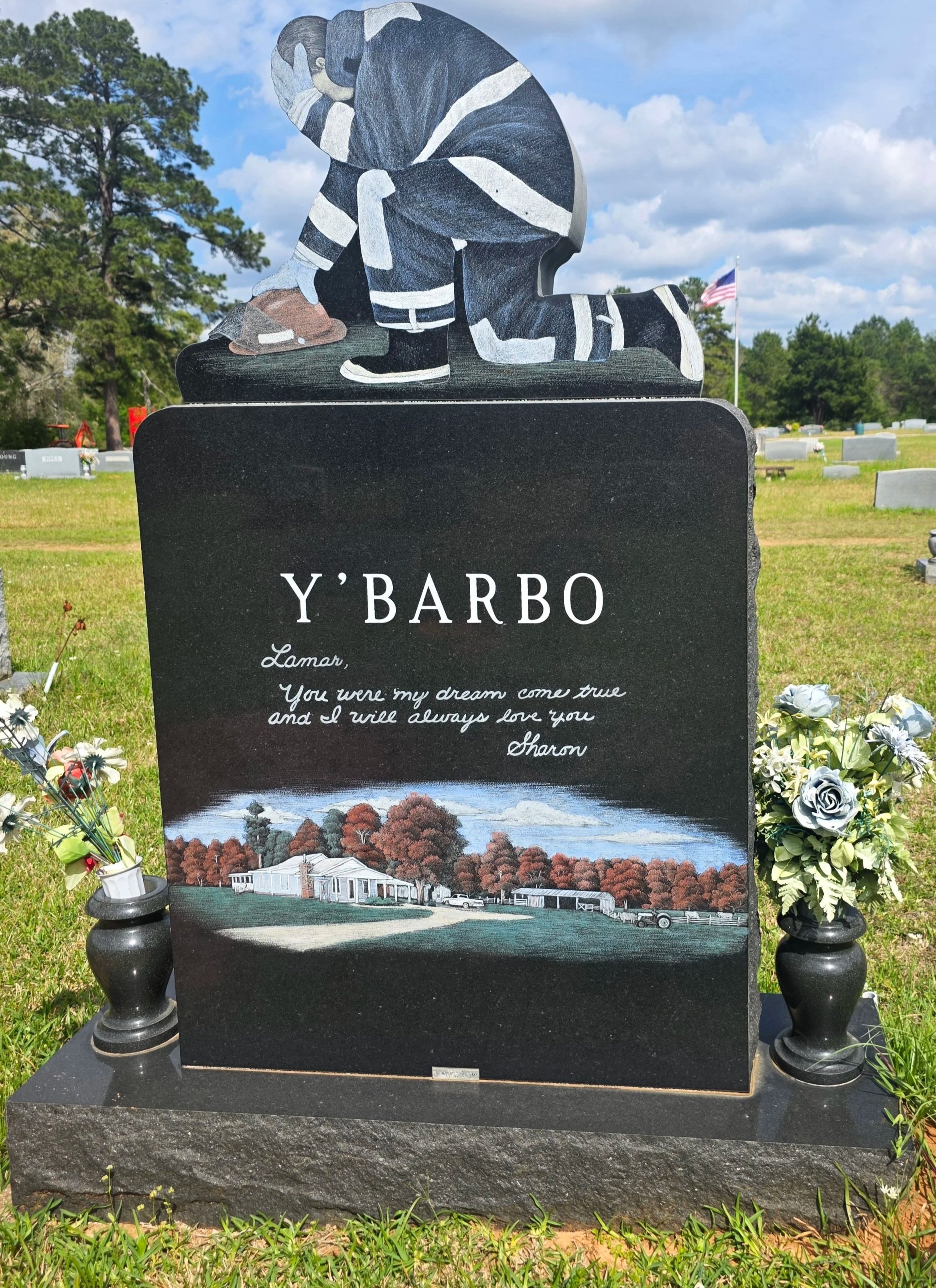 Gravestone with painted illustration of a person in a uniform kneeling and praying, flowers on either side.