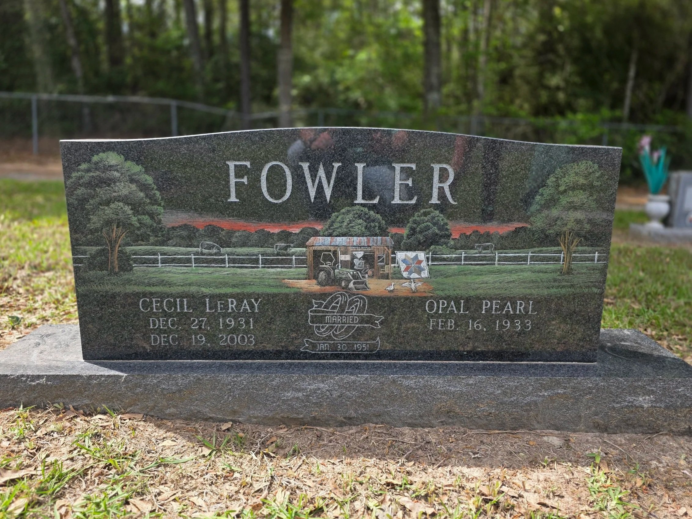 Colorful headstone with a rural scene of trees, a sunset, a truck, and a windmill.