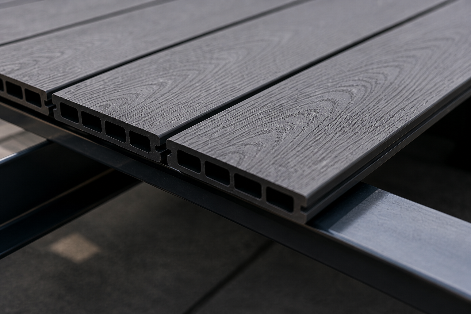 Close-up of a gray composite deck board with a wood grain texture, resting on a black metal frame.