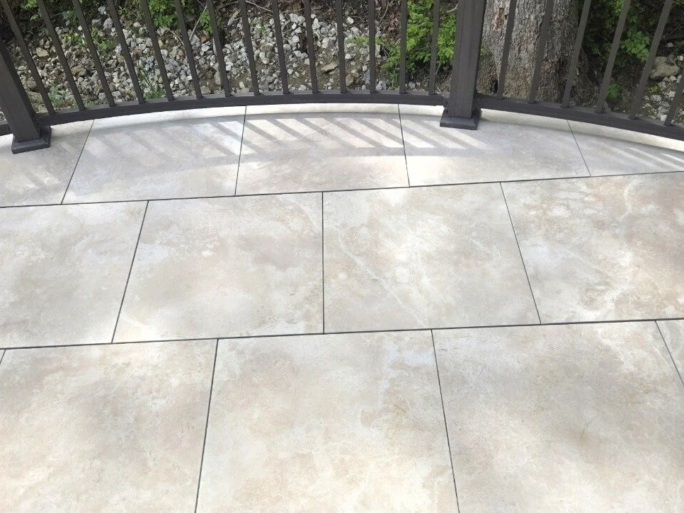 Mbrico porcelain tile deck surface with a curved edge and black metal picket railing, ground visible below