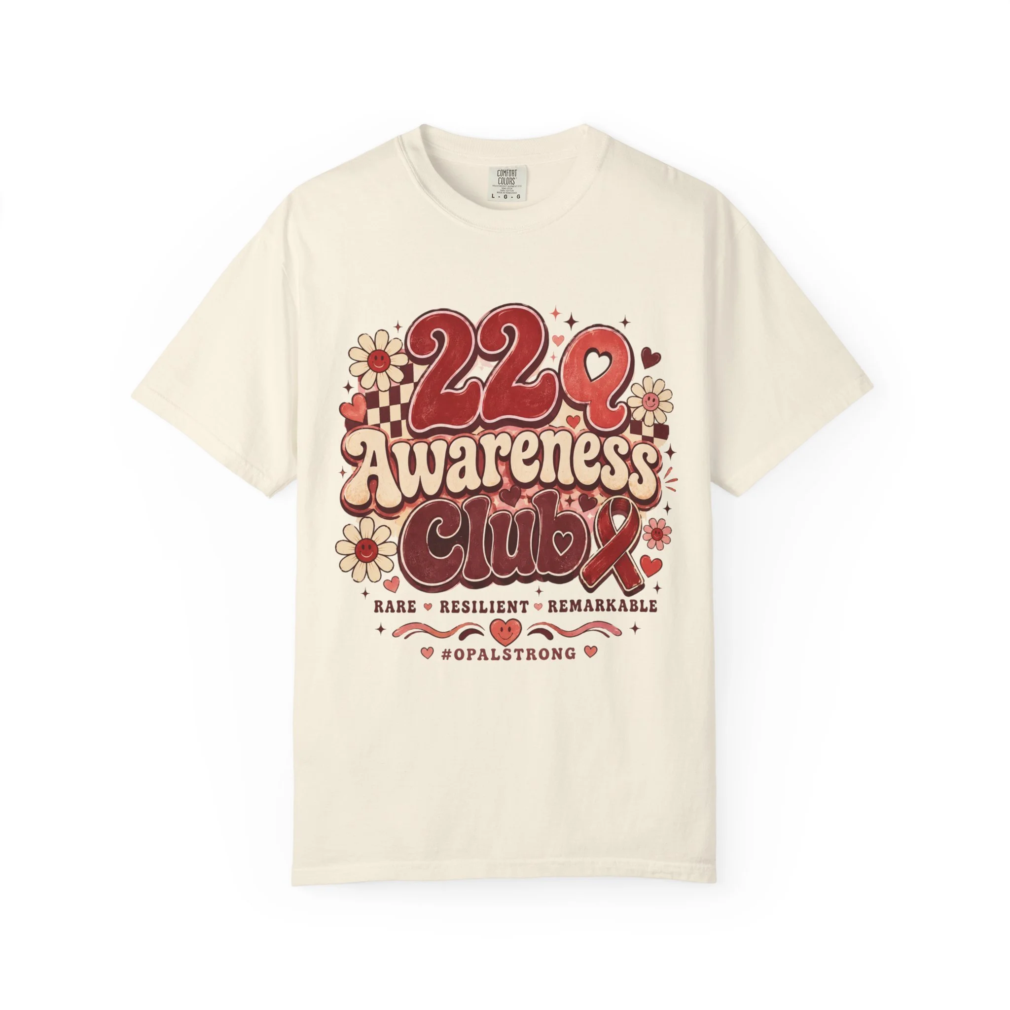 A soft, garment-dyed tee that wears like an old favorite while carrying a heartfelt message. This relaxed-fit shirt features a warm, retro-inspired print that reads “22q Awareness Club” surrounded by cheerful daisies and hand-lettered accents — a gen
