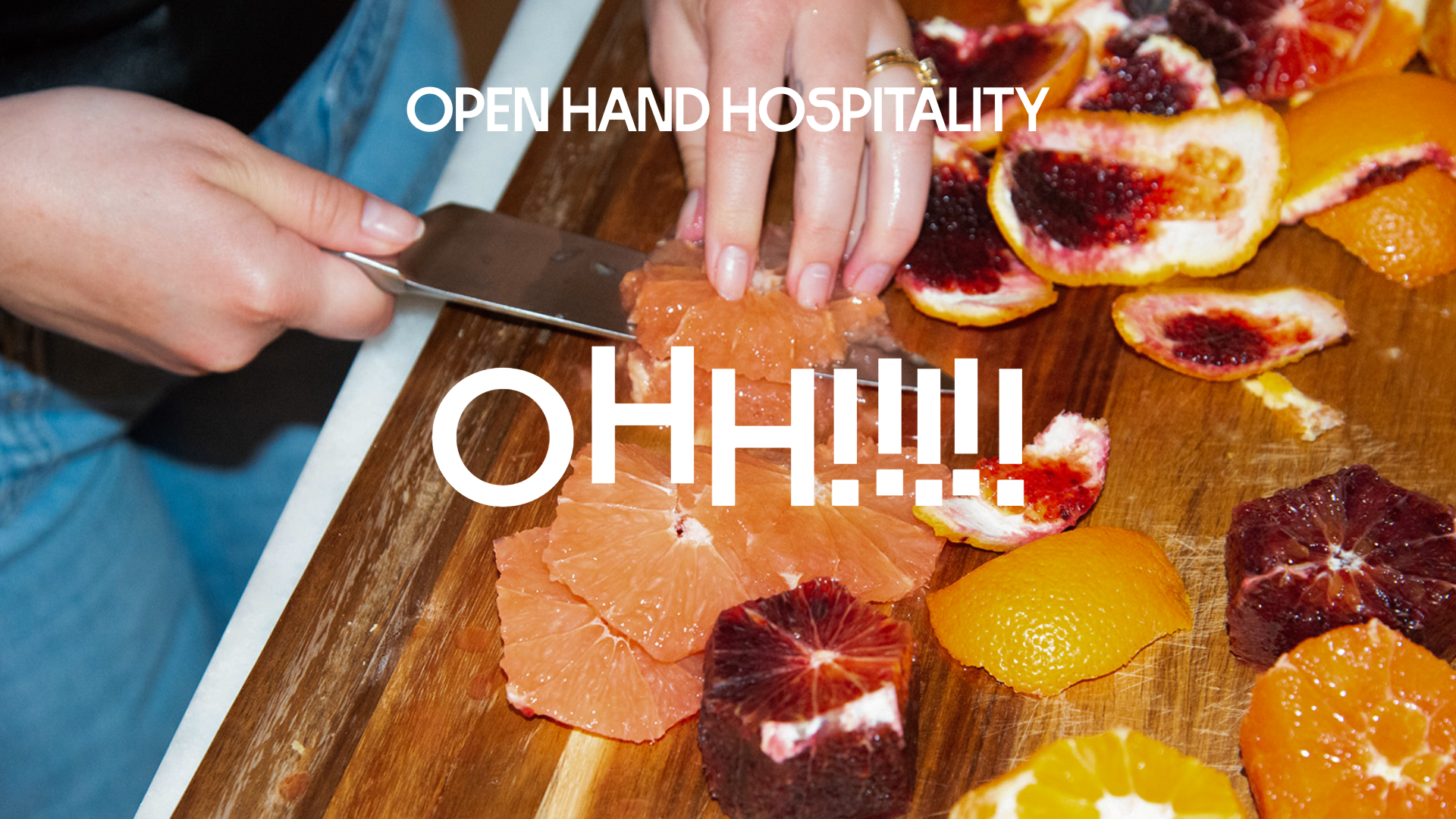 Person slicing grapefruit on a wooden cutting board with various citrus fruit peels and slices, with white text overlay saying "OPEN HAND HOSPITALITY" and "OH!!!!".