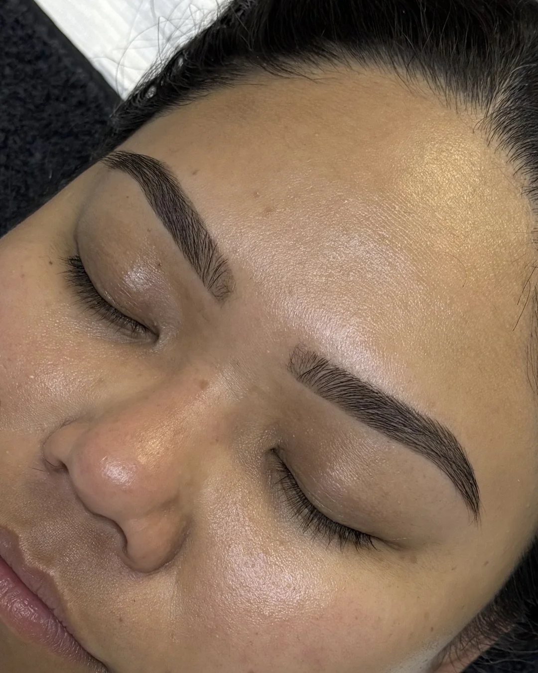 Close-up of a woman's face showing freshly done eyebrow tinting, with her eyes closed, smooth skin, and natural makeup.