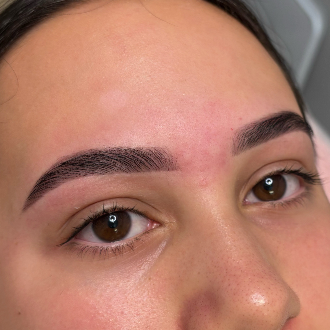 Close-up of a woman's face showing freshly done eyebrow microblading or permanent makeup with well-defined, arched eyebrows and clear skin.