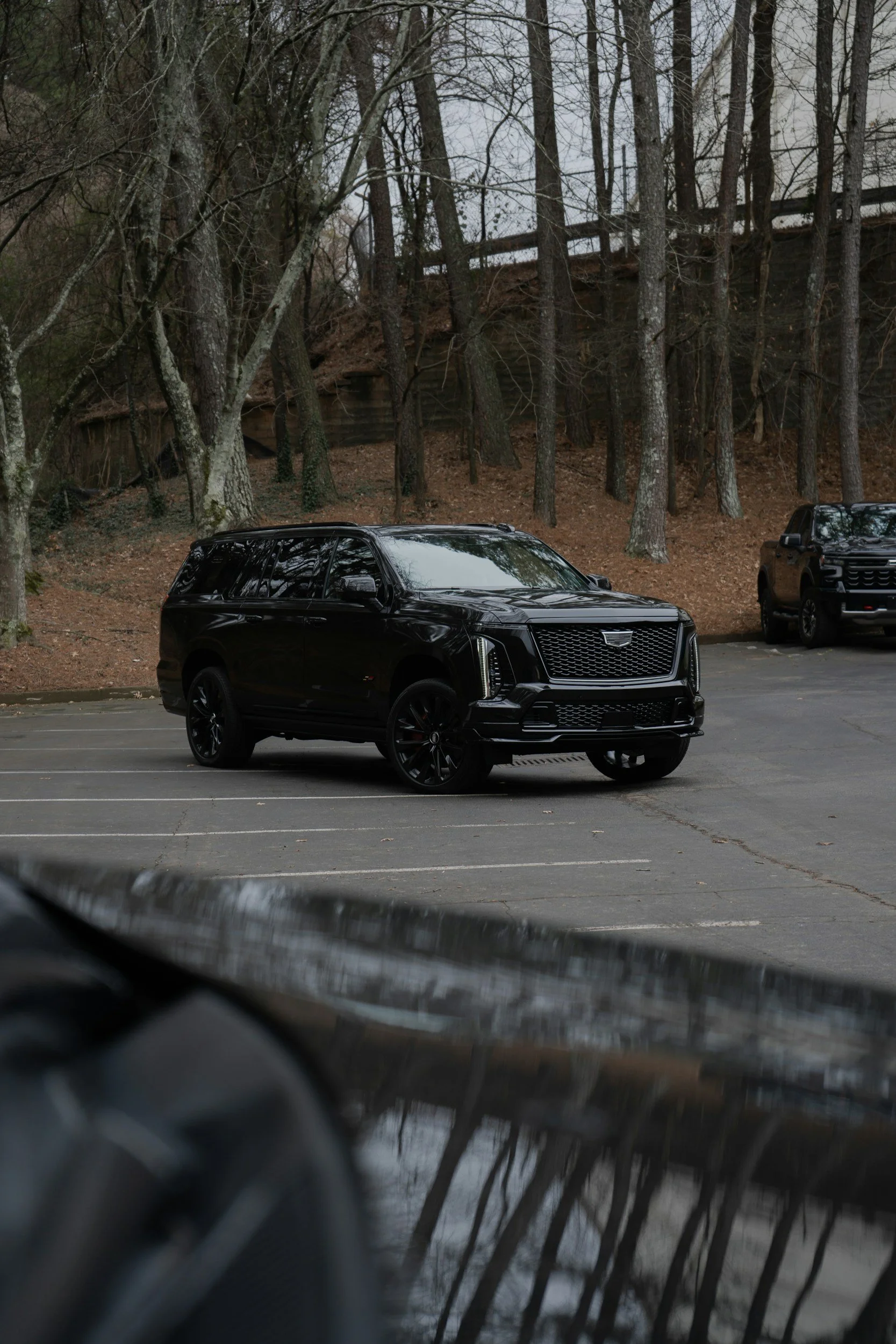 A black luxury SUV parked in an empty parking lot with trees and a hillside in the background.