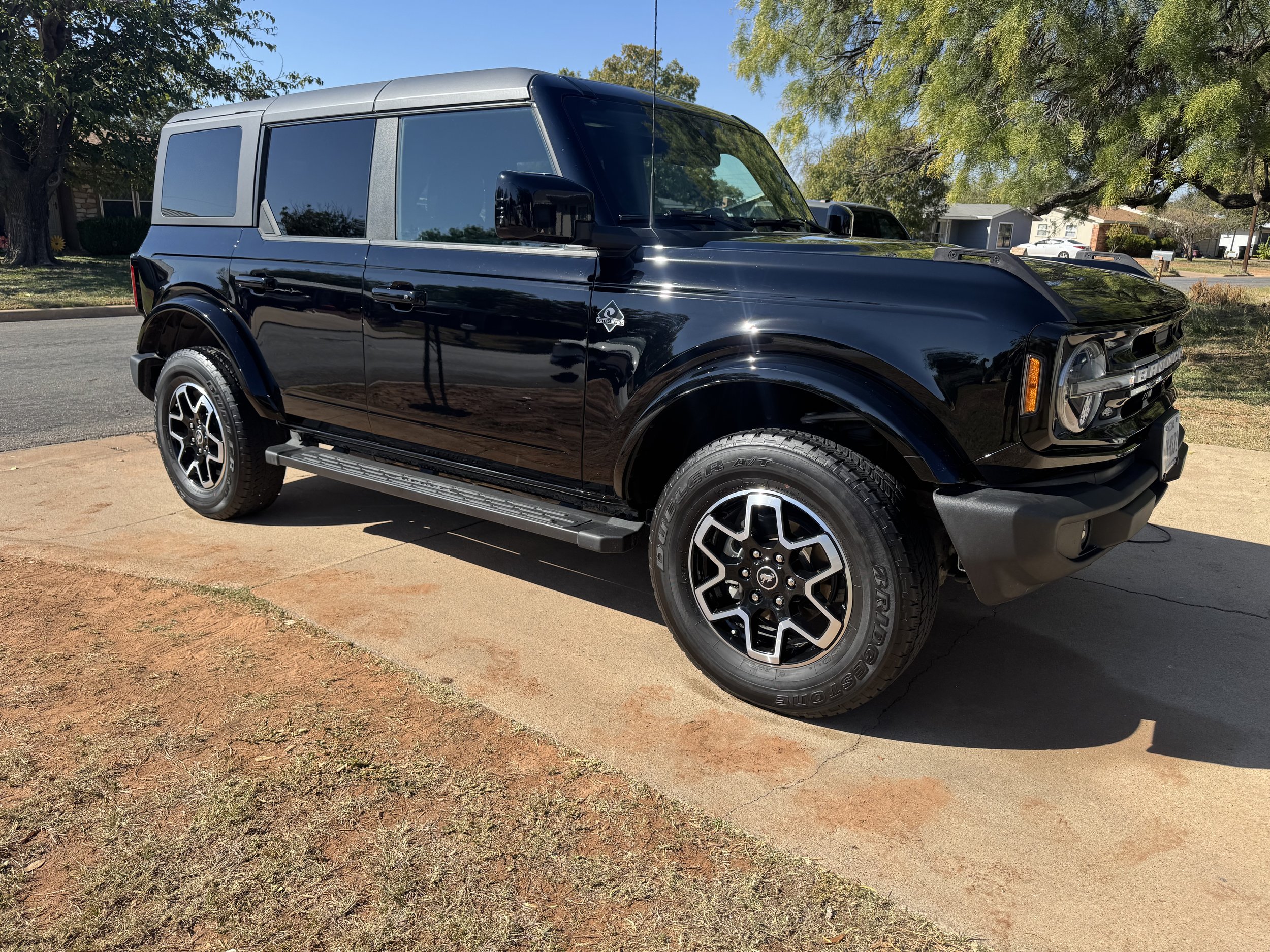 Black SUV parked on a concrete driveway with trees and houses in the background.