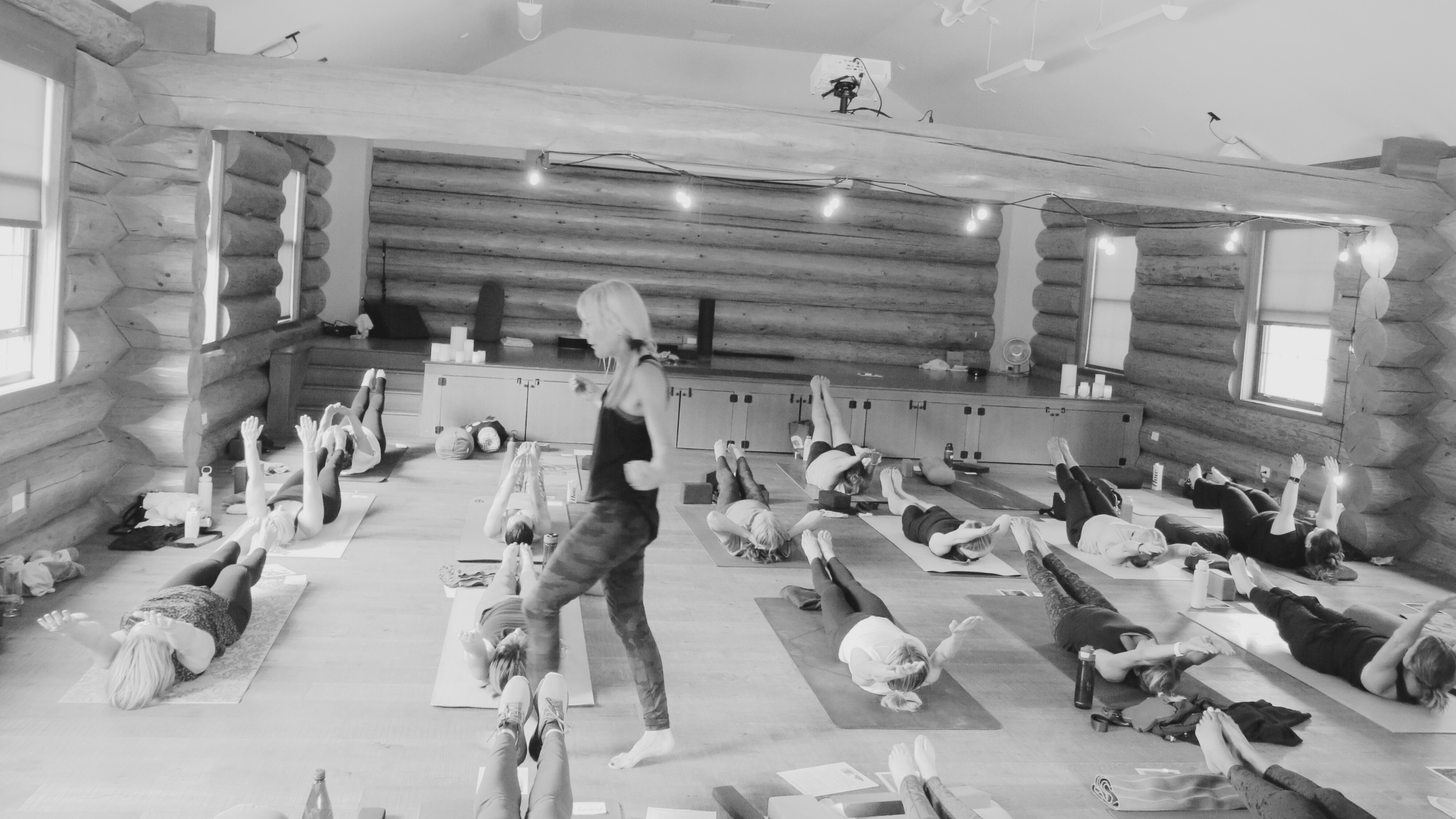Group of people participating in a yoga class in a rustic wooden studio, lying on yoga mats and practicing relaxation poses.