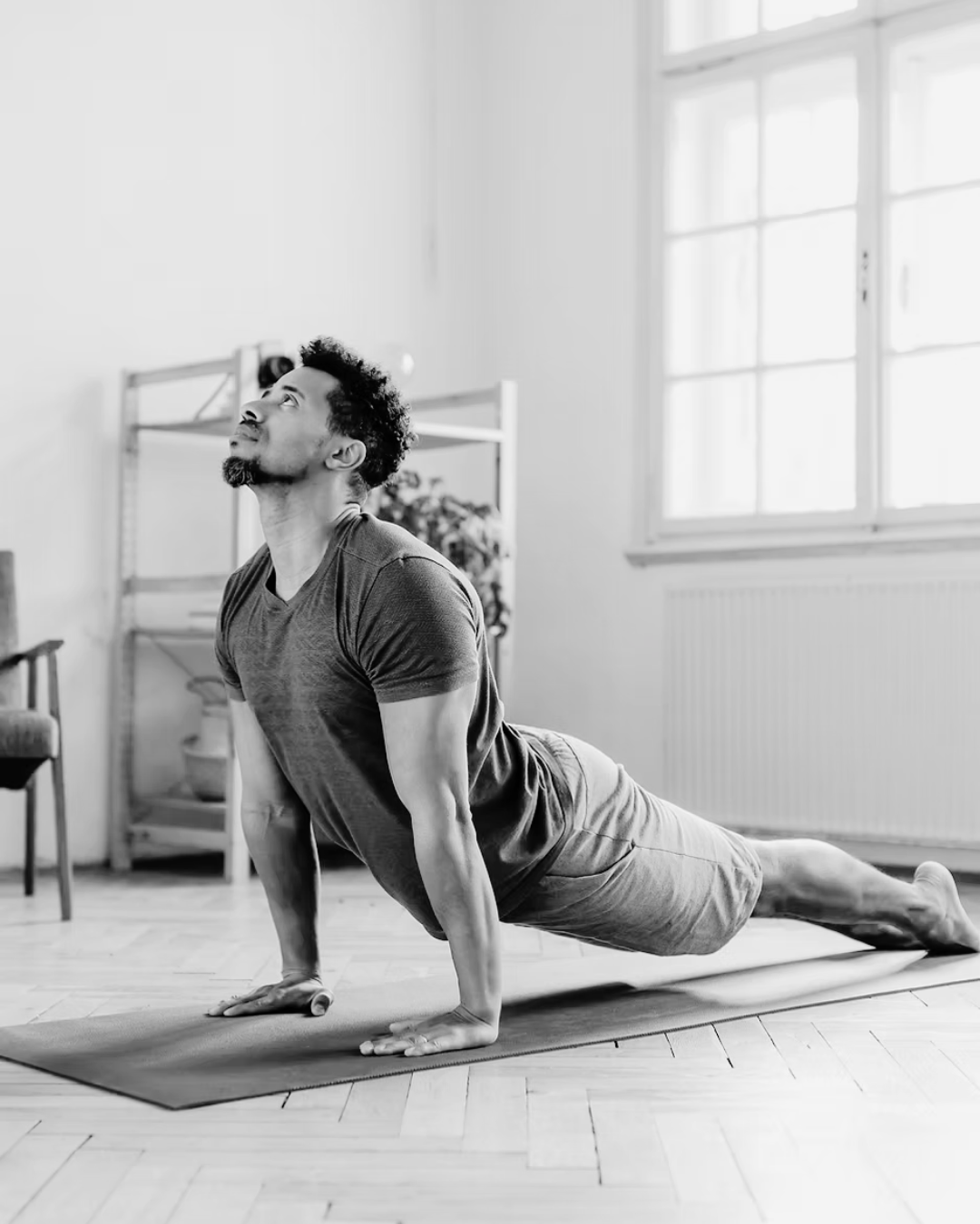 Man practicing yoga in a room with large windows, performing a plank pose on a mat.
