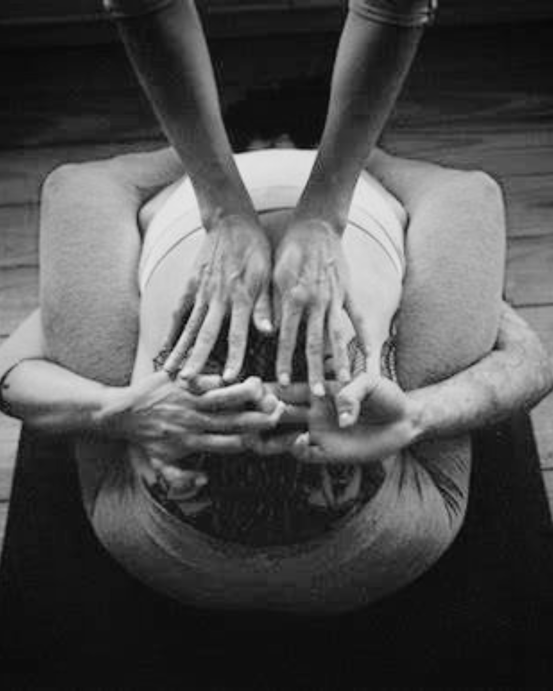 Two yoga instructors demonstrating a partner pose, with one person on the ground and the other person kneeling on top, supporting their partner's legs and hands.
