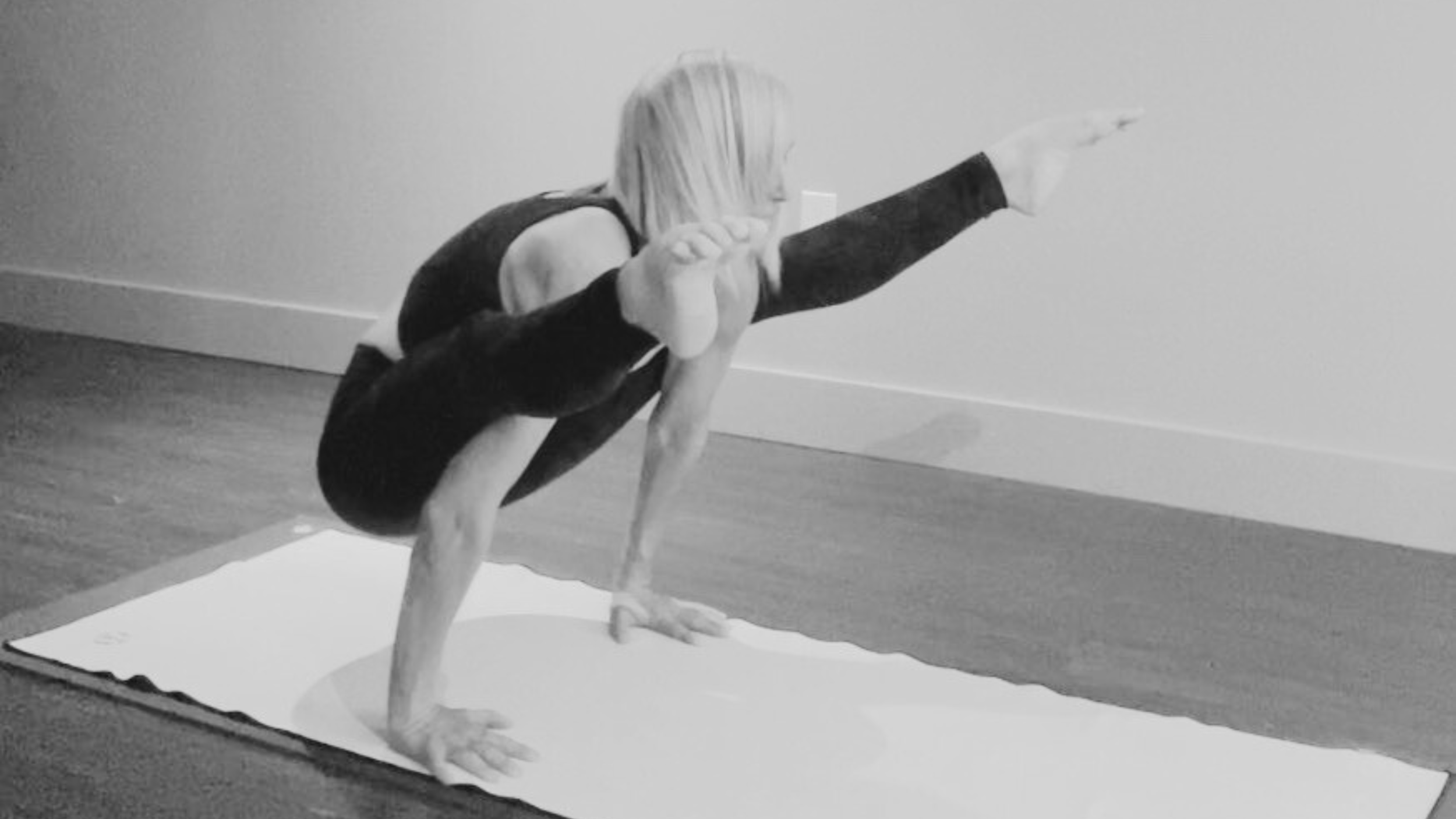 An Authorized Yoga Instructor in Calgary, Jan Goranson, performing a forearm balance yoga pose on a white yoga mat indoors.