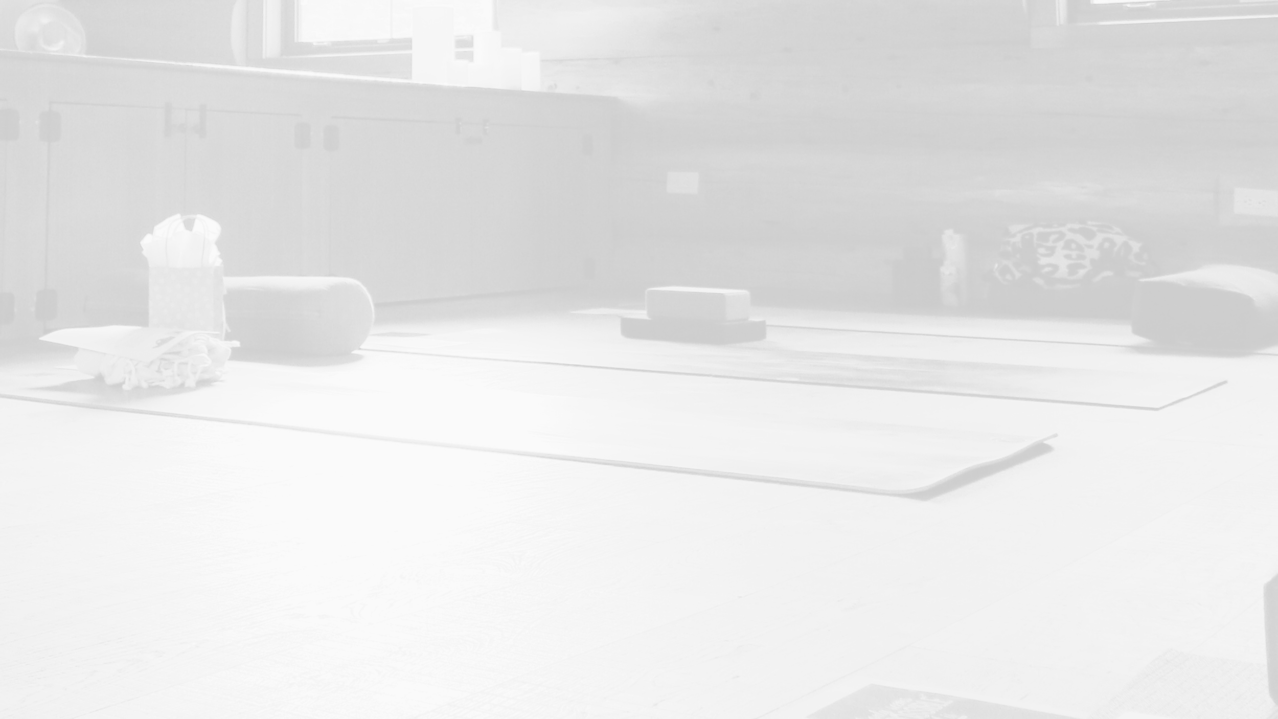 Yoga mat on floor with a yoga block, a water bottle, an eye pillow, and a blanket nearby in a room with wooden wall paneling.