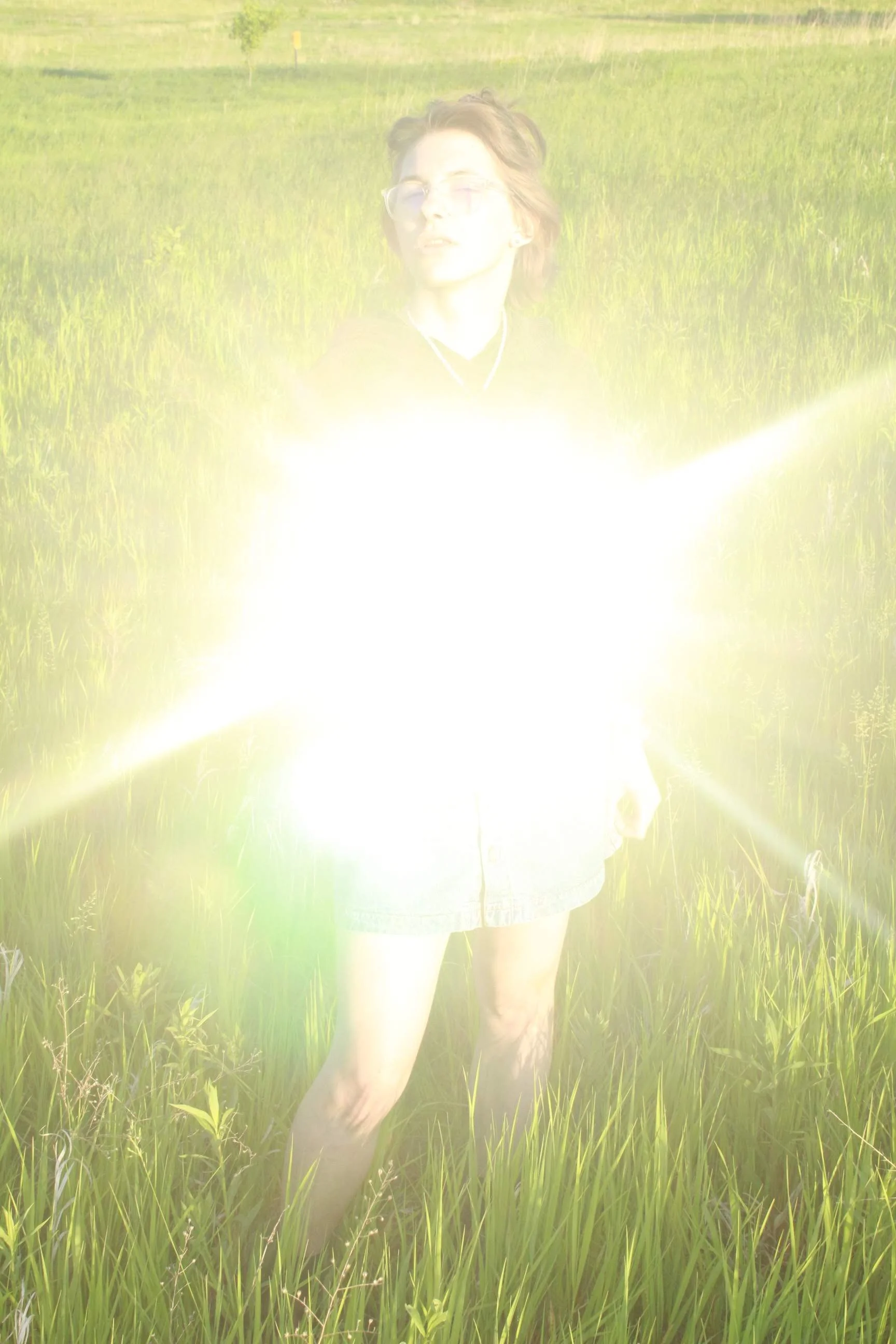 A person standing in a grassy field with a bright, overexposed flash or light in front of them, making their face and body partially obscured.
