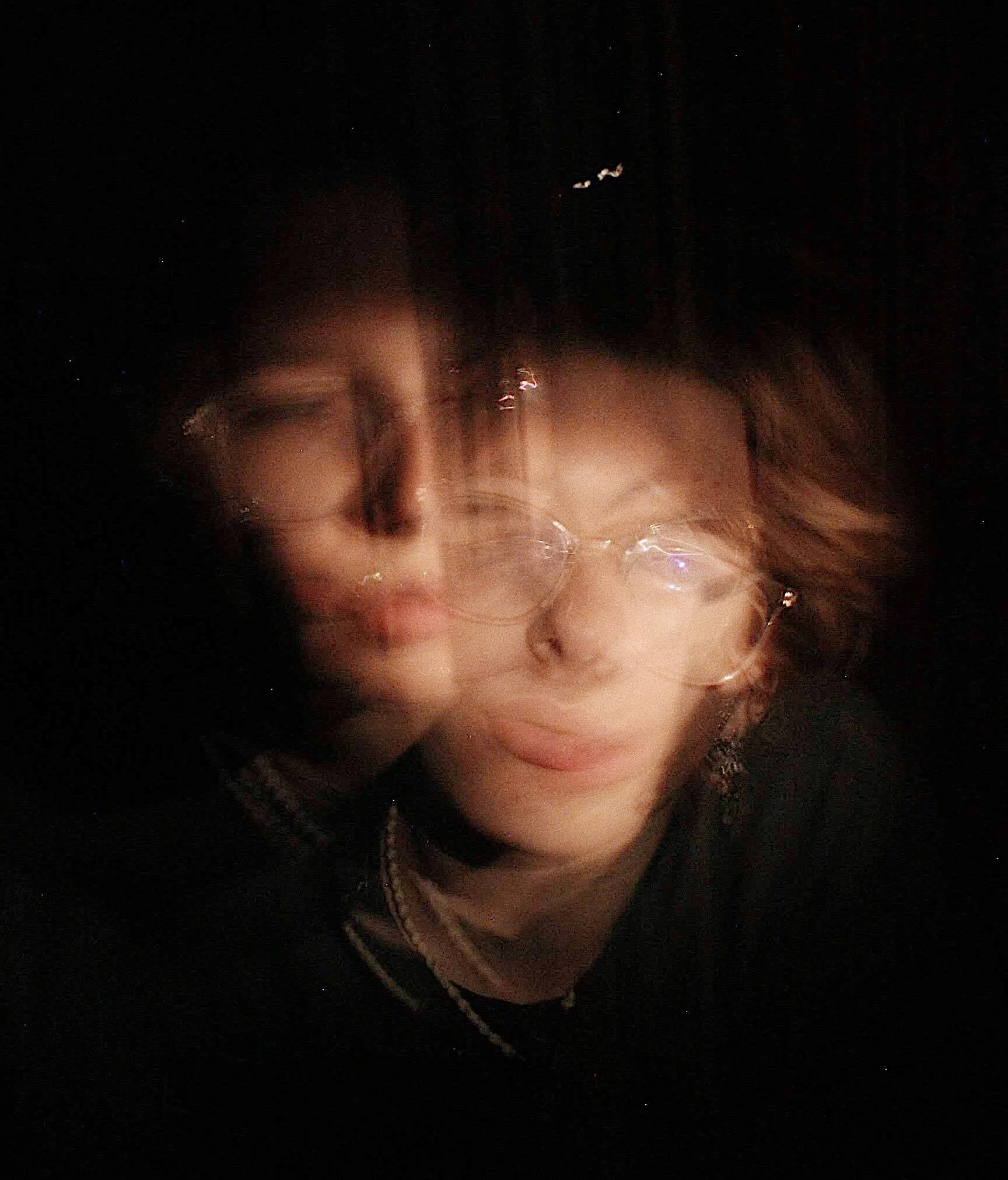 A blurry photo of a person with glasses and short hair, with dual exposure effect creating a ghost-like double image.