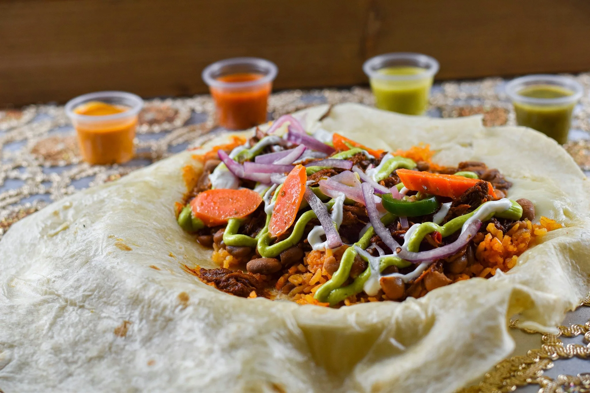 A serving of Mexican-style layered dip on a tortilla chip with vegetables and sauces in small cups.