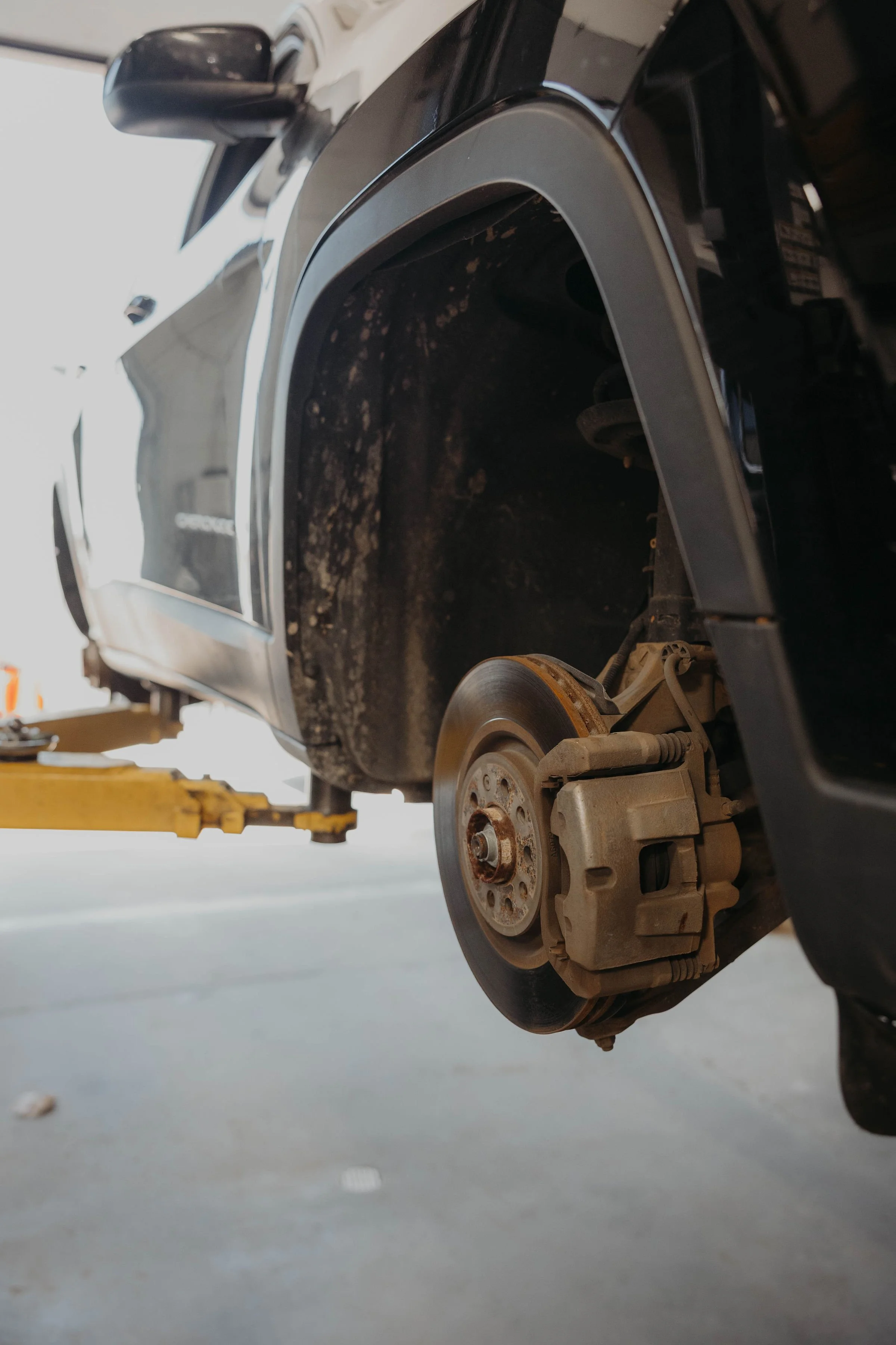A close-up view of a car's front wheel removed for repair in a garage, with the brake disc and suspension components visible.