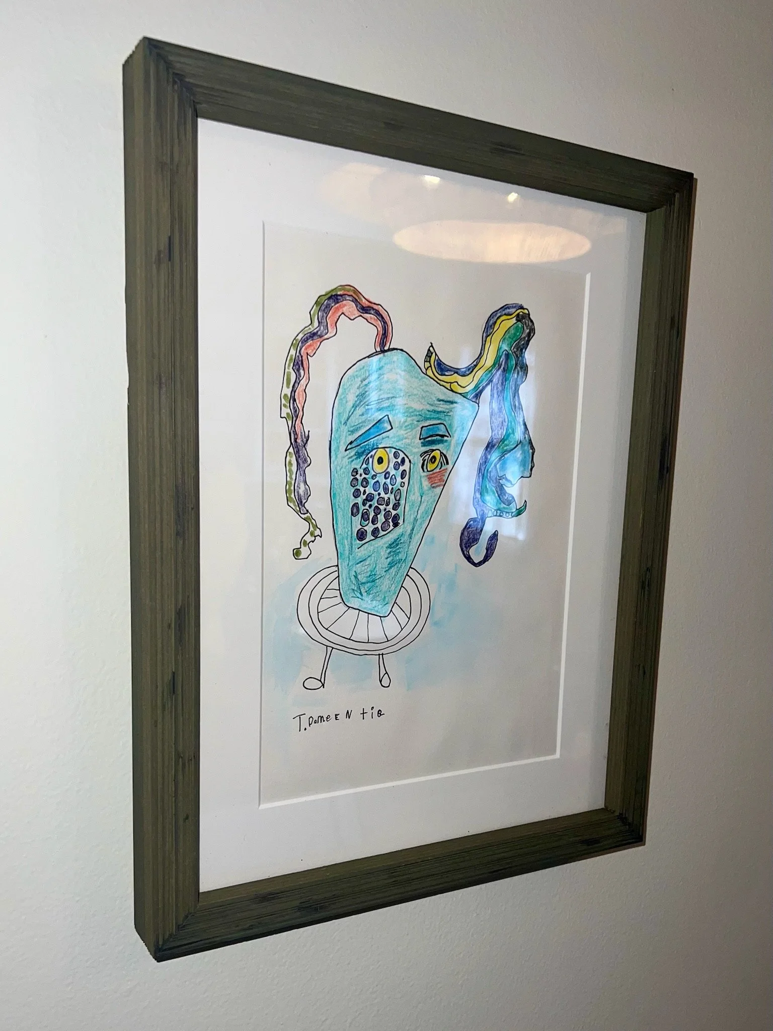 Framed artwork featuring a colorful, abstract drawing of a face with multicolored hair, large expressive eyes, and the signature 'T. Doméntie' at the bottom.