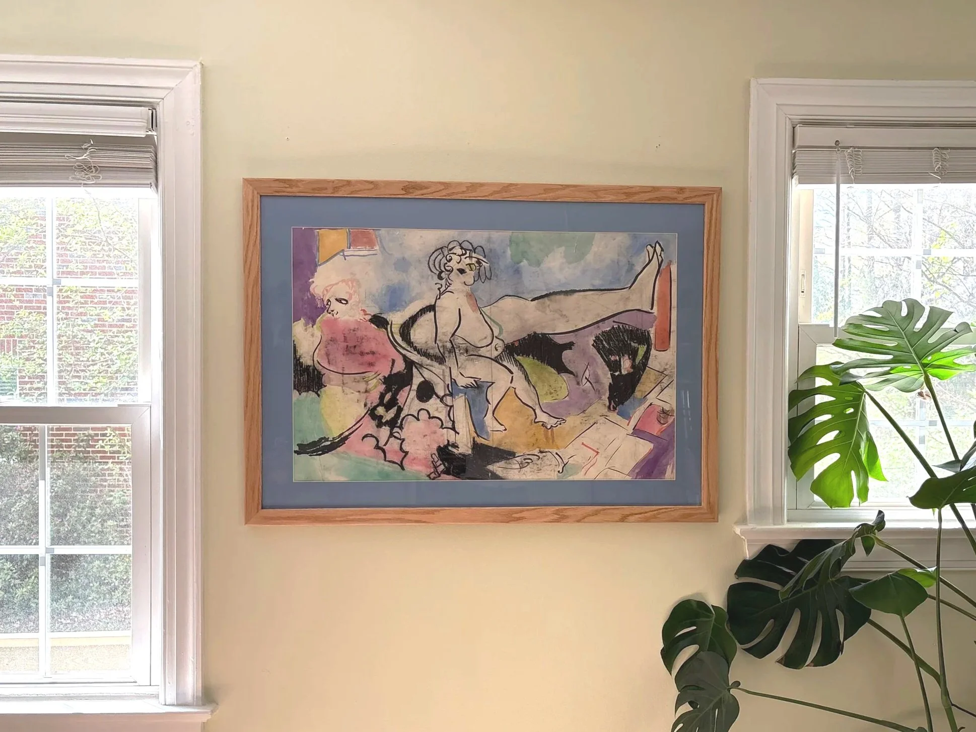 An abstract colorful painting hangs on a yellow wall between two windows. There is a large green Monstera plant in the lower right corner.