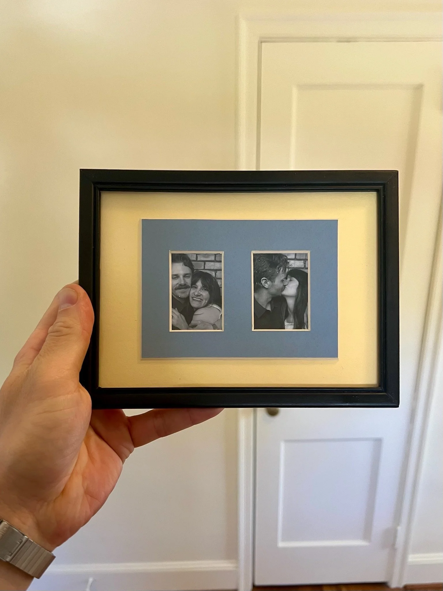 A person holding a framed black and white photo of a man and woman in a close embrace, with a brick wall background.