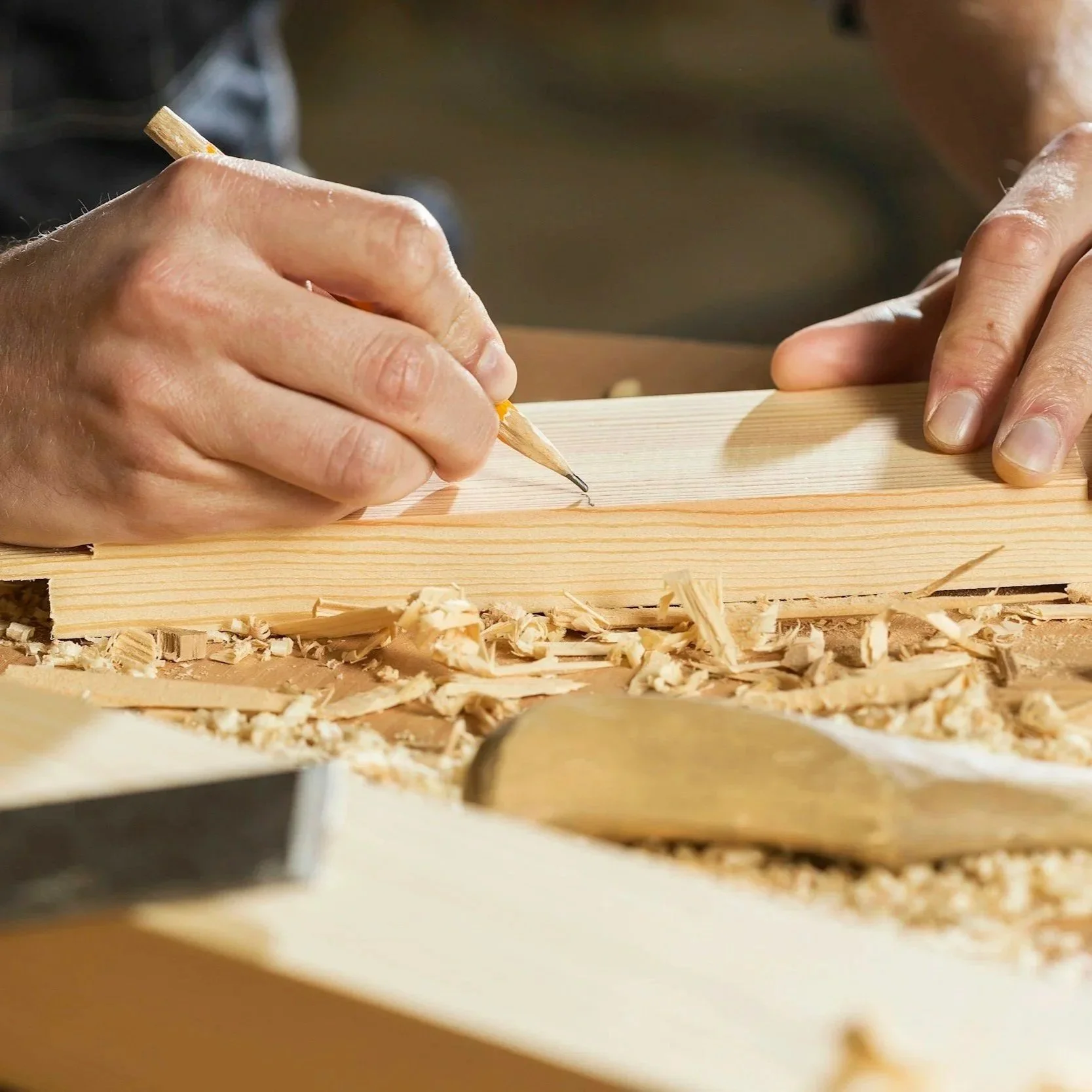 Close-up of a person carving wood with a pencil, surrounded by wood shavings.