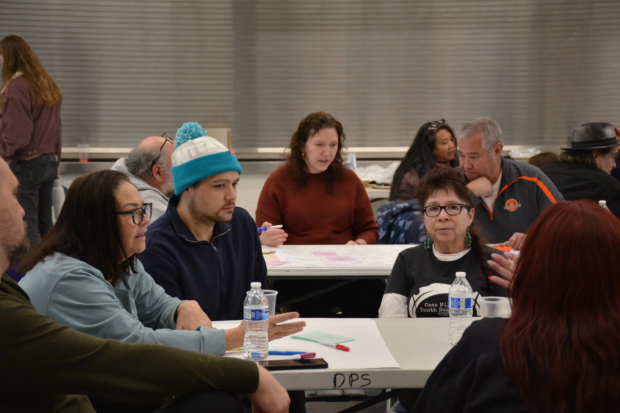 People sitting at a round table having a discussion during a meeting or workshop in a well-lit indoor space.